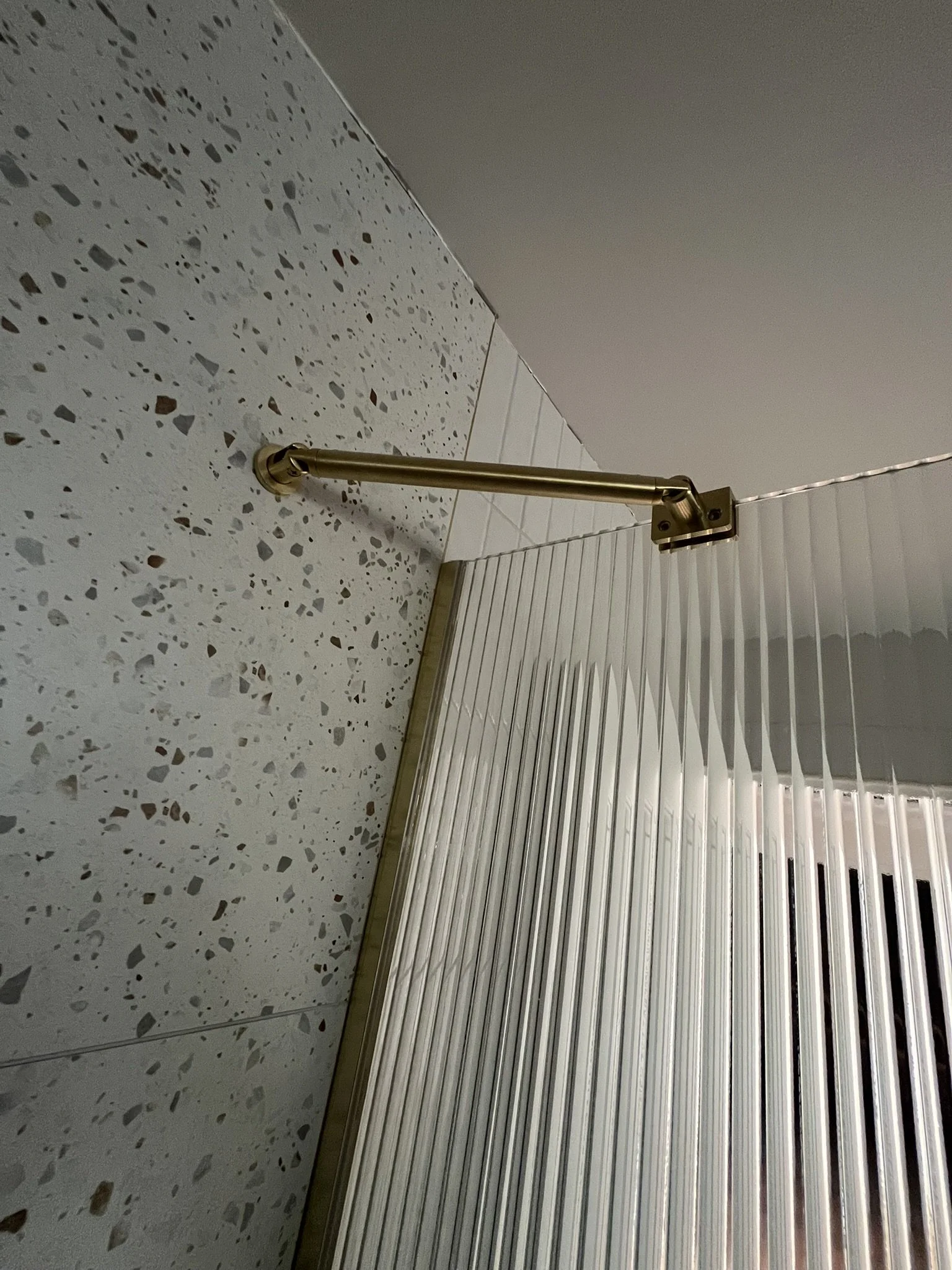 A view of a terrazzo floor with a brass railing and vertical white blinds covering a window or door.