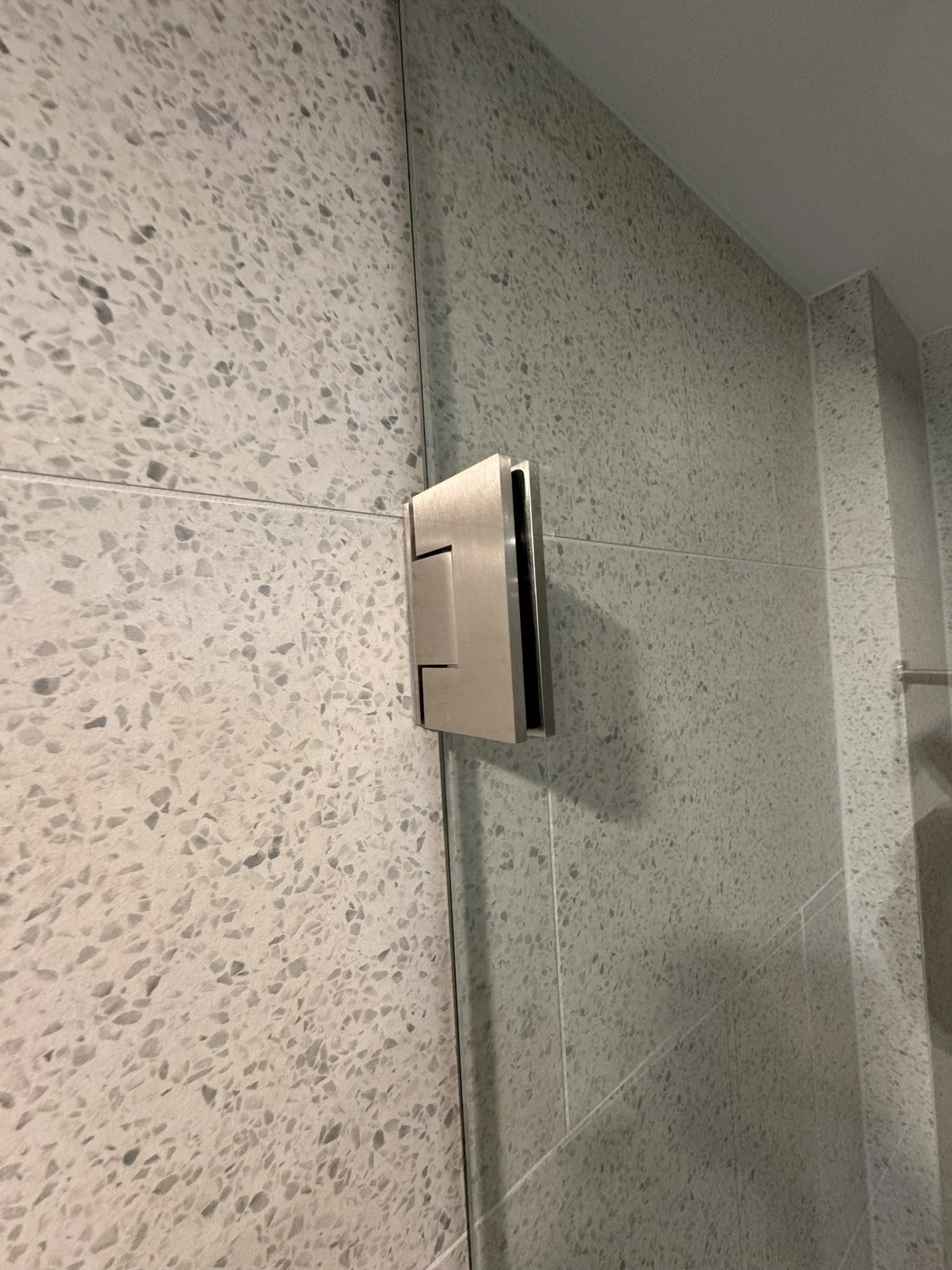 Close-up of a metallic flush plate on a terrazzo-tiled wall, likely in a bathroom or restroom.