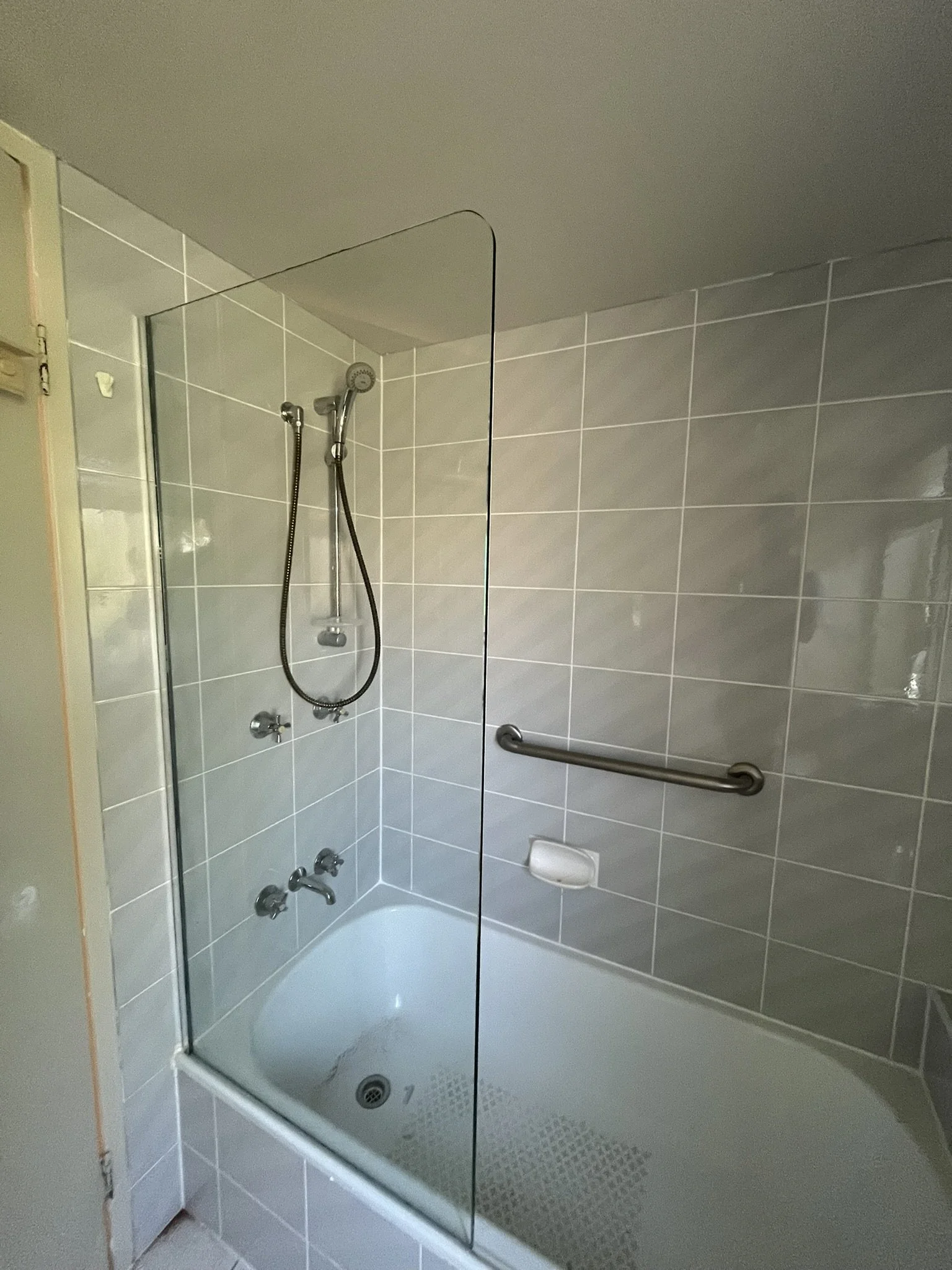Shower with a glass partition, handheld shower head, and tiled walls in a bathroom.
