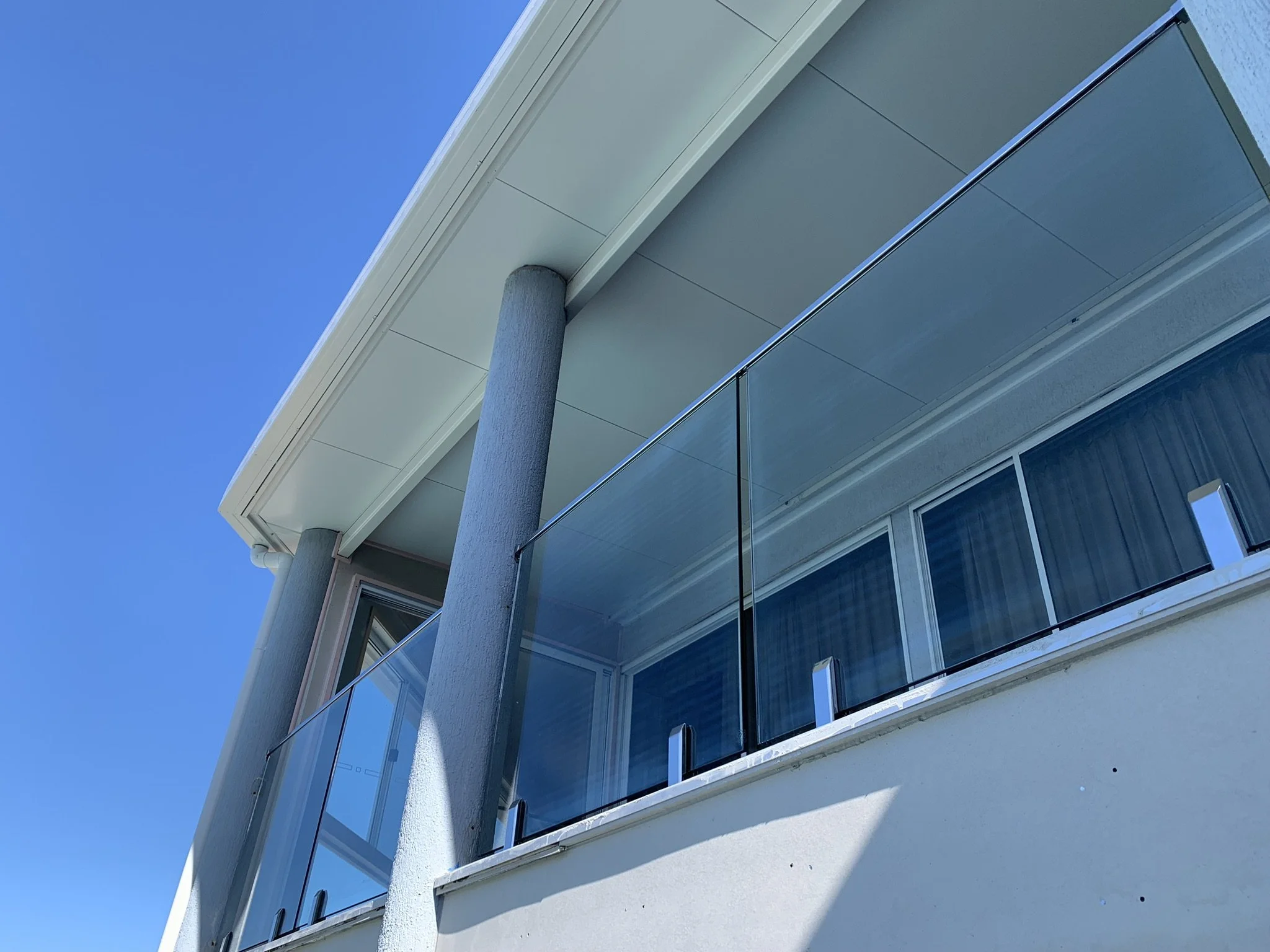 A modern building with glass balconies, supported by cylindrical pillars, against a clear blue sky.
