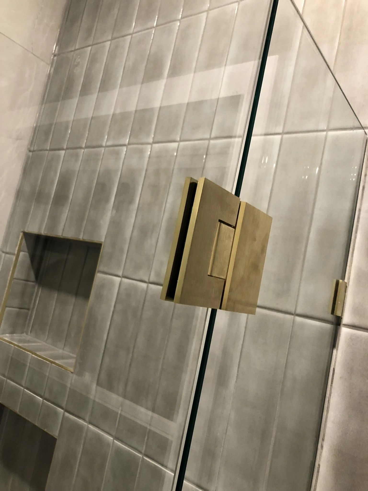 A mirror reflecting a tiled wall and a small wooden shelf.