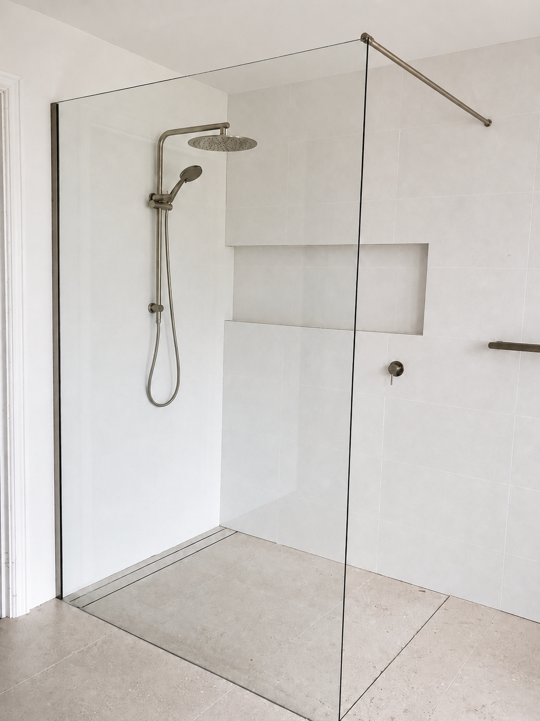 Bathroom shower with glass enclosure, silver showerhead, and white tiled walls.