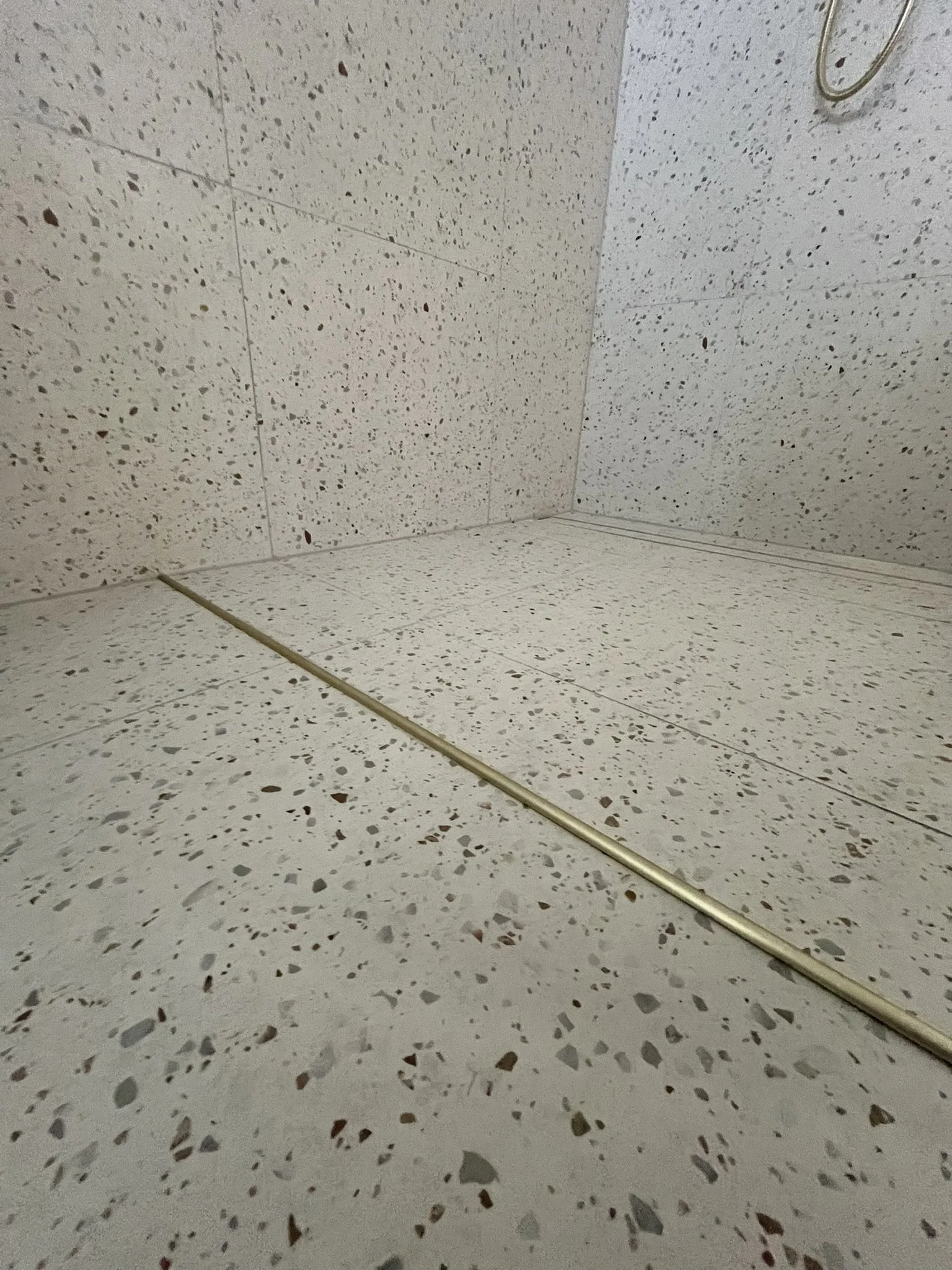 A terrazzo floor and wall with beige and brown speckles, and a brass or gold-colored metal strip running along the floor.