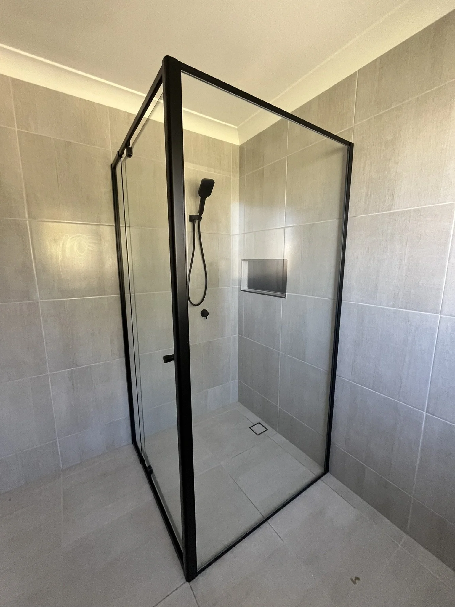 A modern bathroom shower with glass walls, a black showerhead, and beige tiled walls.