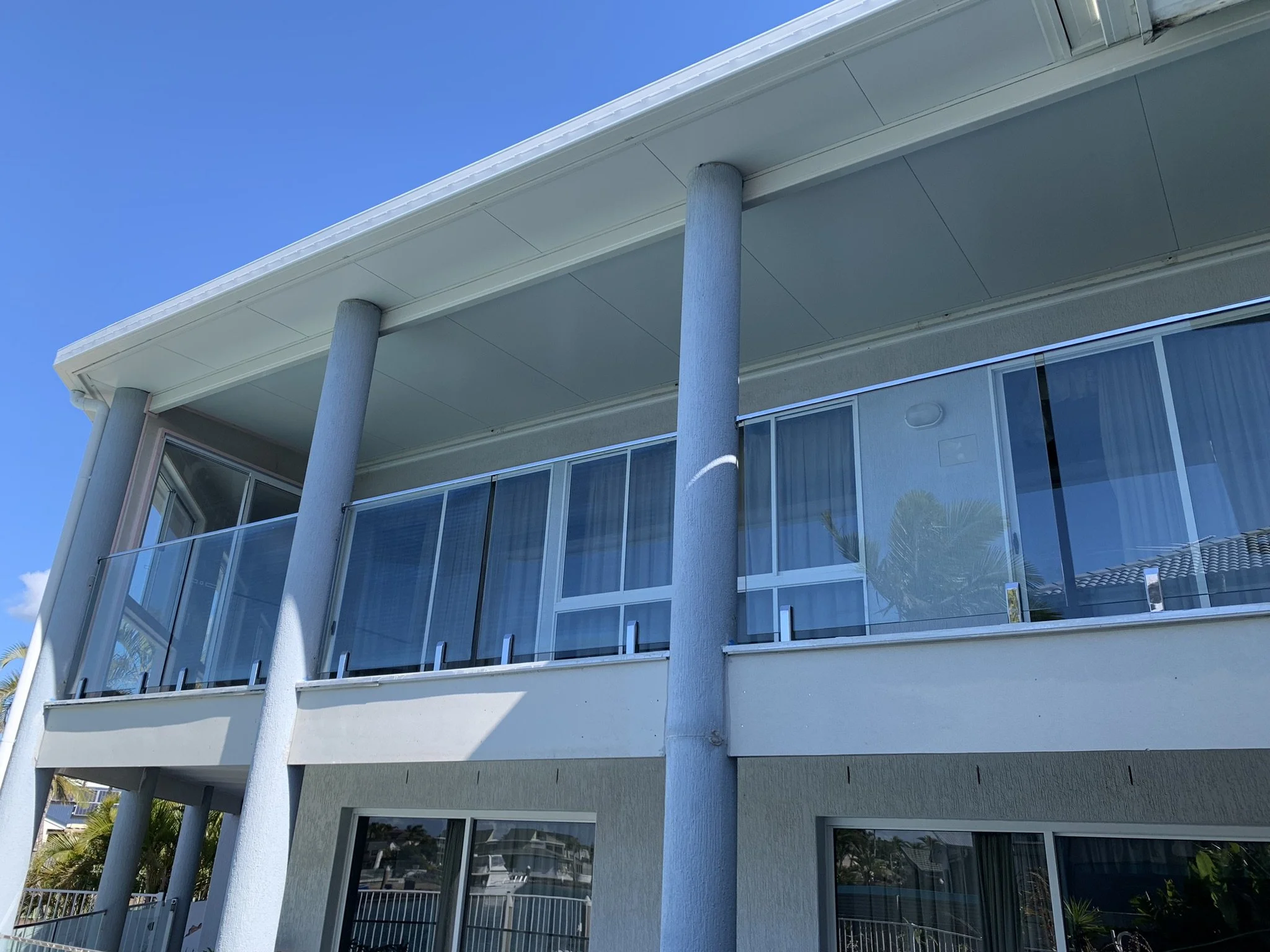 View of a modern multi-story building with large glass windows, white exterior walls, supported by white columns, with a clear blue sky in the background.