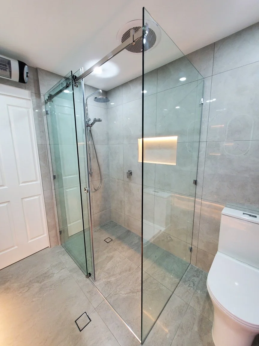 Modern bathroom with a glass shower enclosure, a rainfall showerhead, and a white toilet, featuring gray marble tiles on the walls and floor.