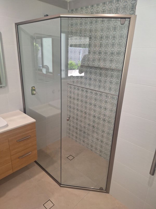 A bathroom shower with a geometric patterned tile wall and glass enclosure.