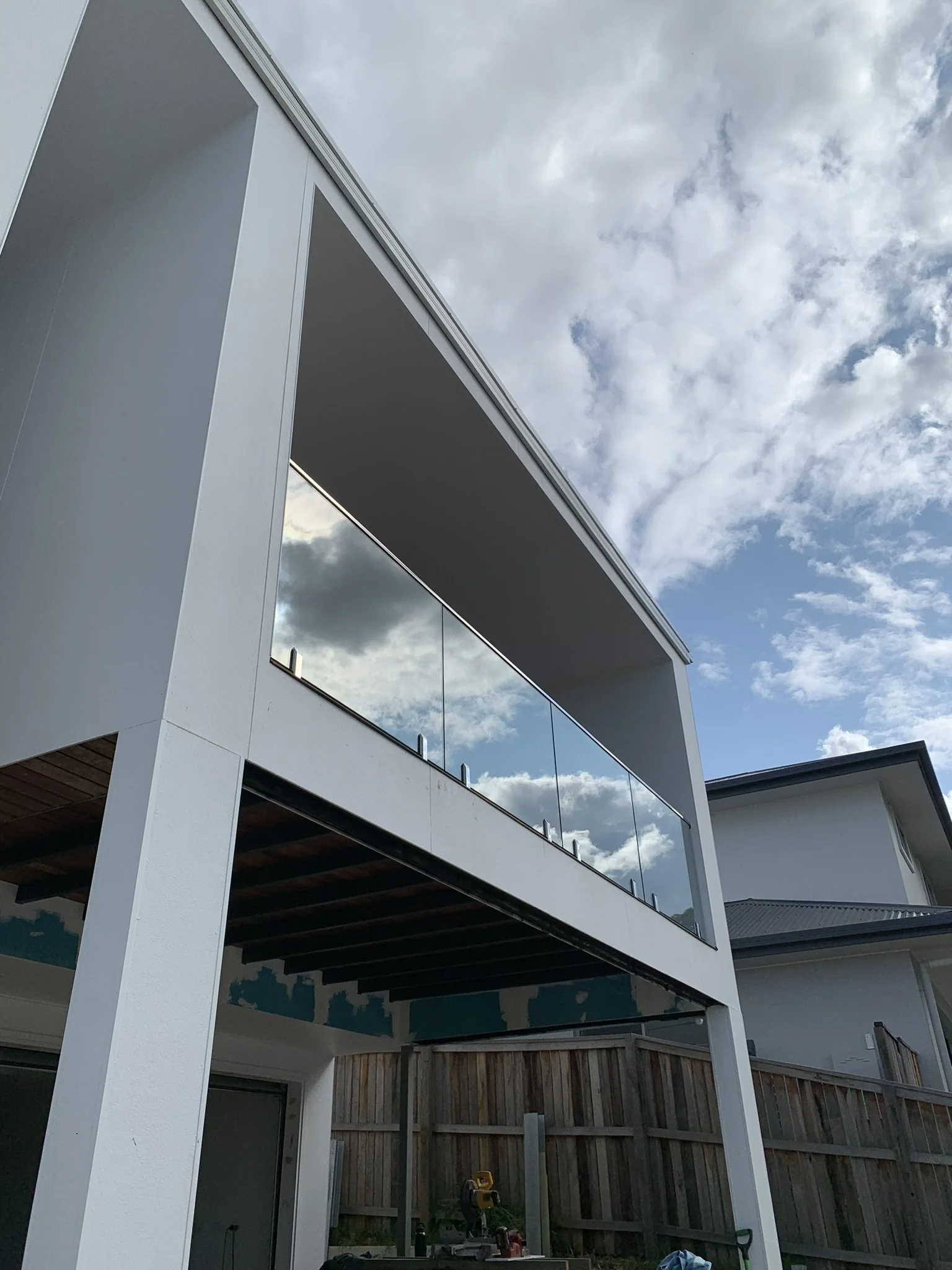 Photo of a modern, white, multi-story building with large glass windows and a balcony, taken outdoors during cloudy weather.