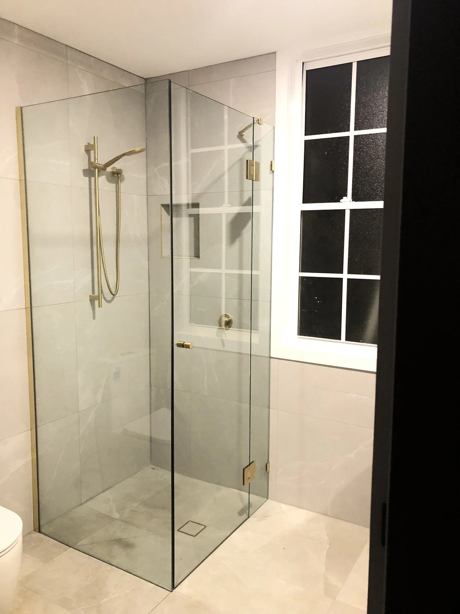 A modern bathroom with a glass-enclosed shower, a window with frosted glass, and minimalist design.