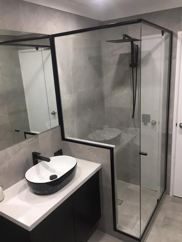 Modern bathroom with a black and white vessel sink, large mirror, and glass-enclosed walk-in shower.