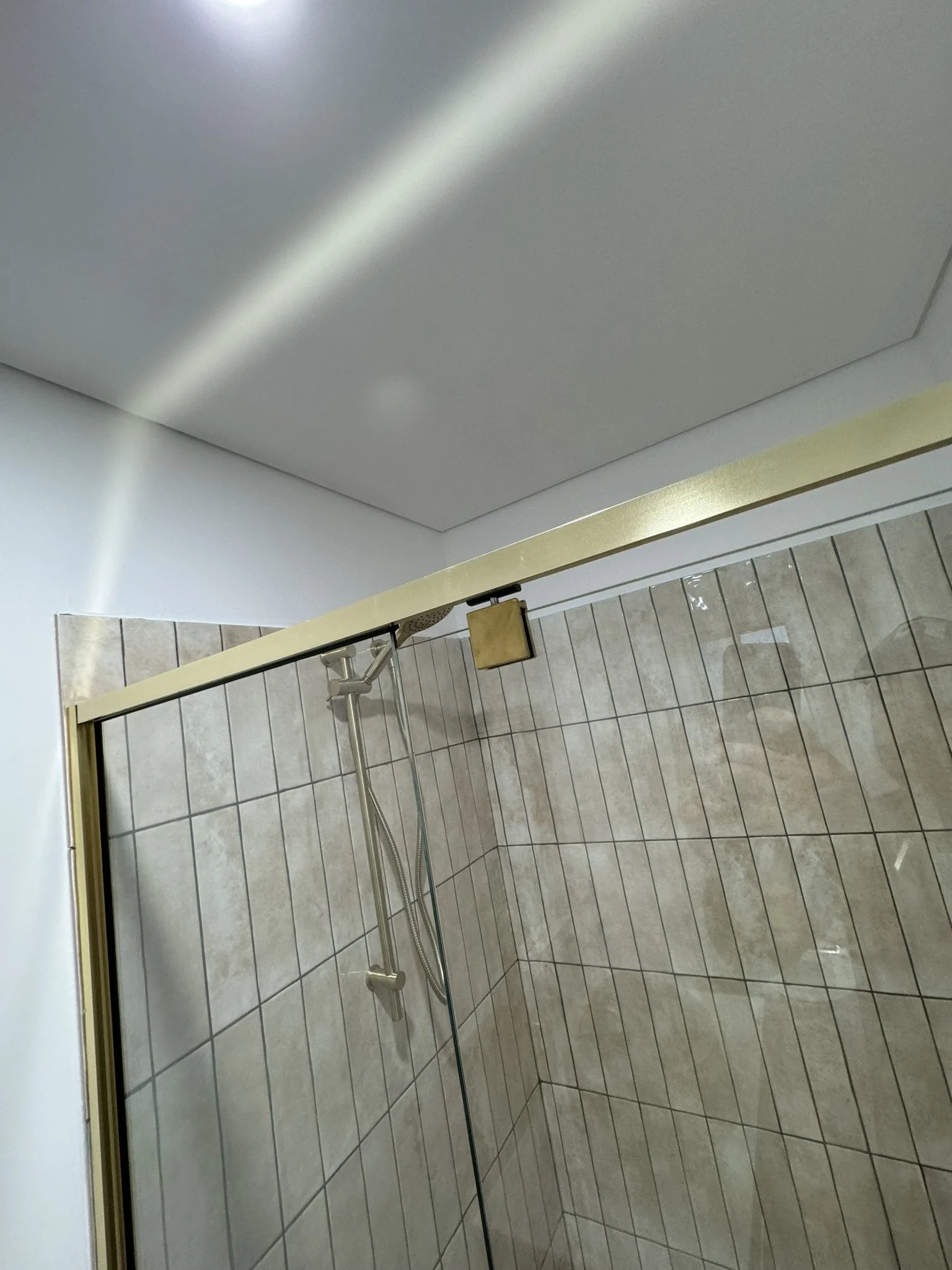 A walk-in shower with beige tiled walls and a glass door, featuring a shower head and a handheld shower attachment.