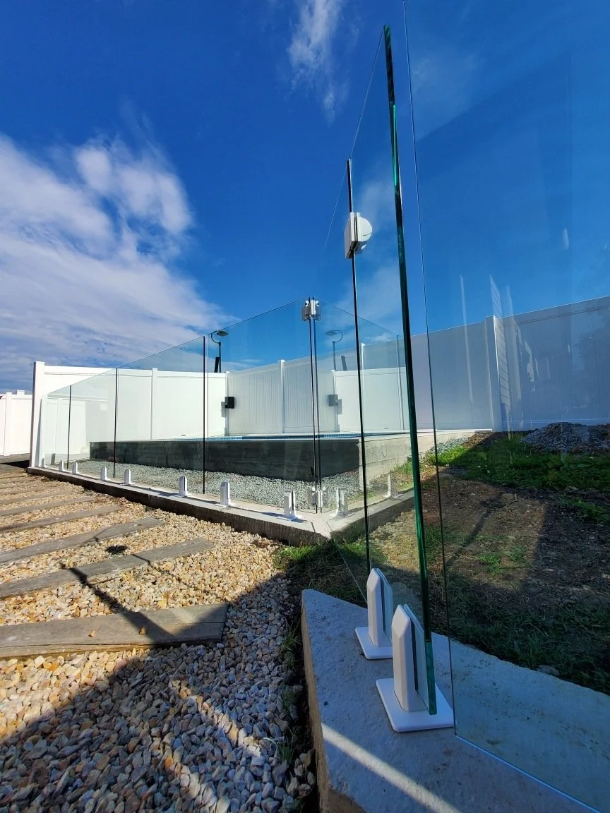 Glass panels supported by white bases, forming a fence or barrier outside, with a clear blue sky in the background.