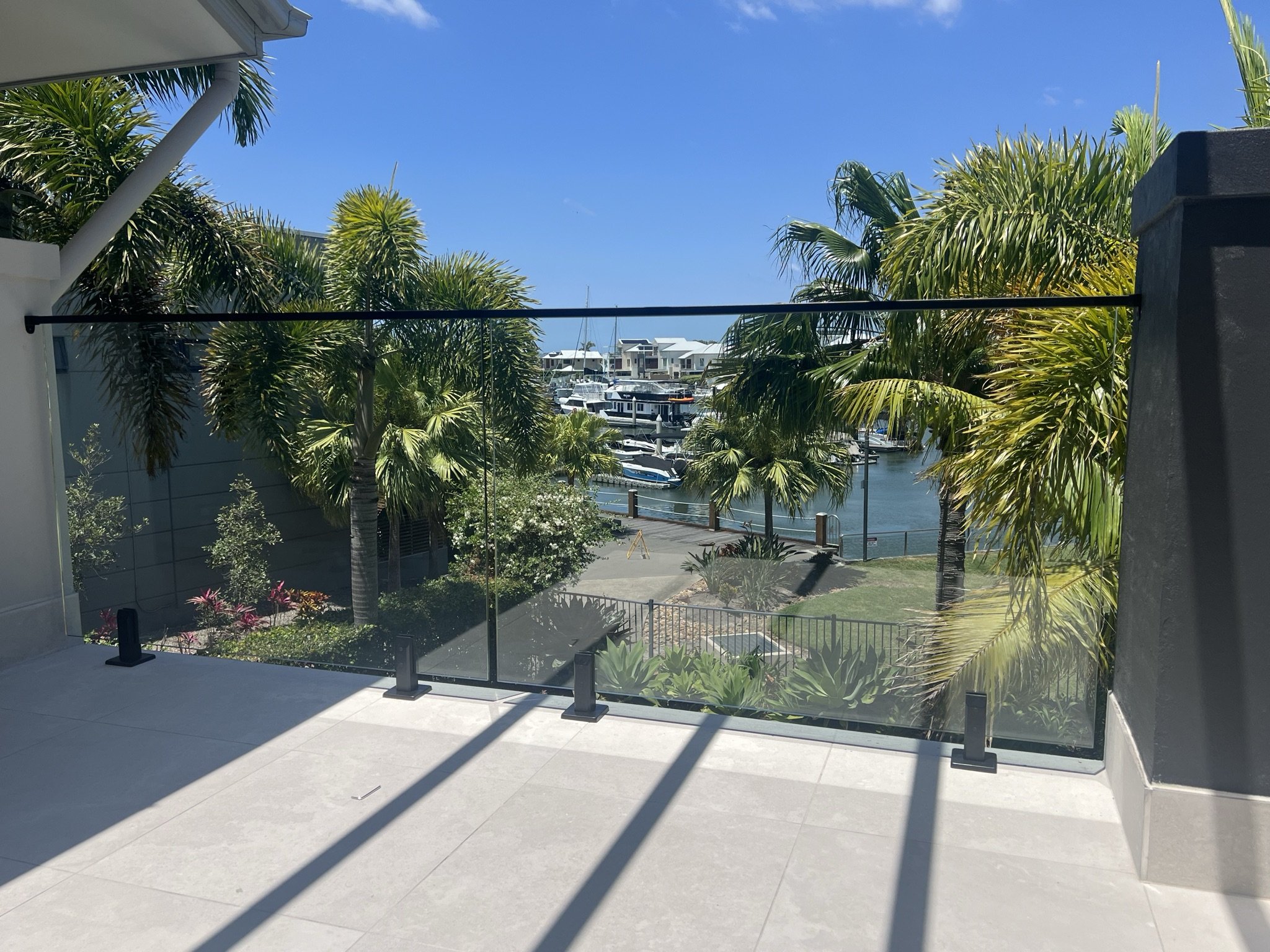 View from a balcony overlooking a marina with boats, surrounded by palm trees and residential buildings under a clear blue sky.