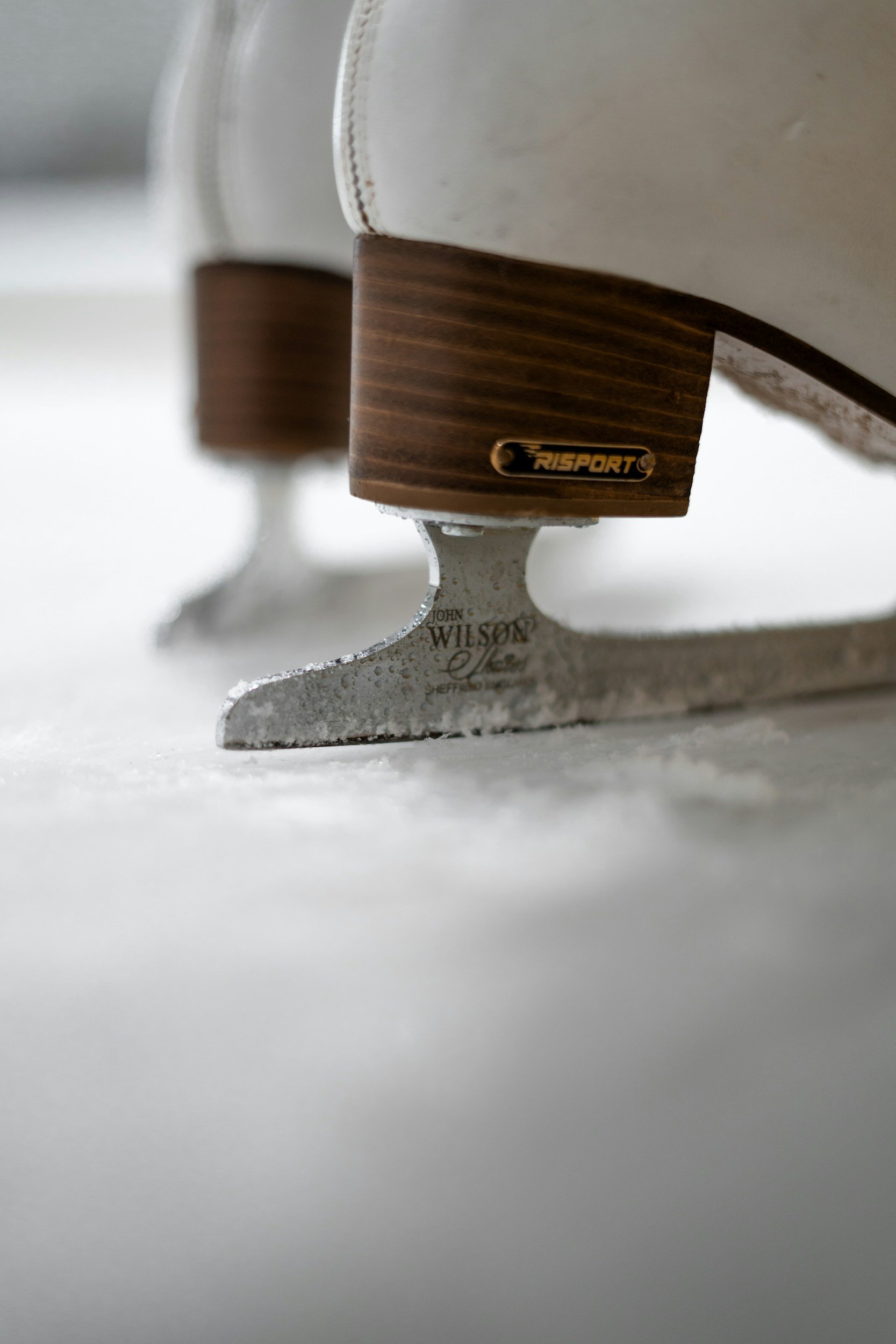 Close-up of a vintage ice skate with a wooden heel and metal blade, showing the brand name 'Risport' on the side.