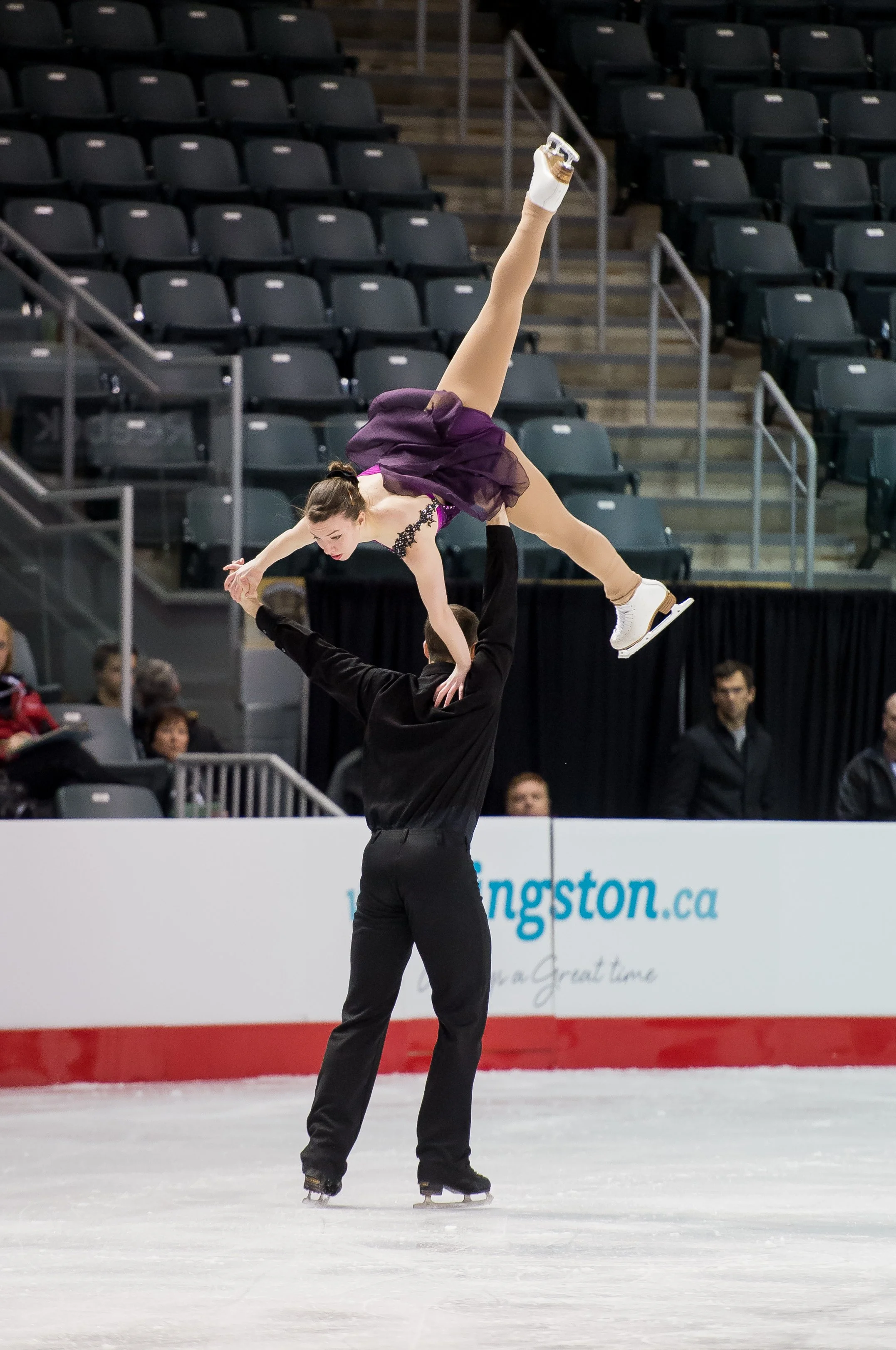 An ice skater performing a lift during a figure skating routine at an indoor arena.