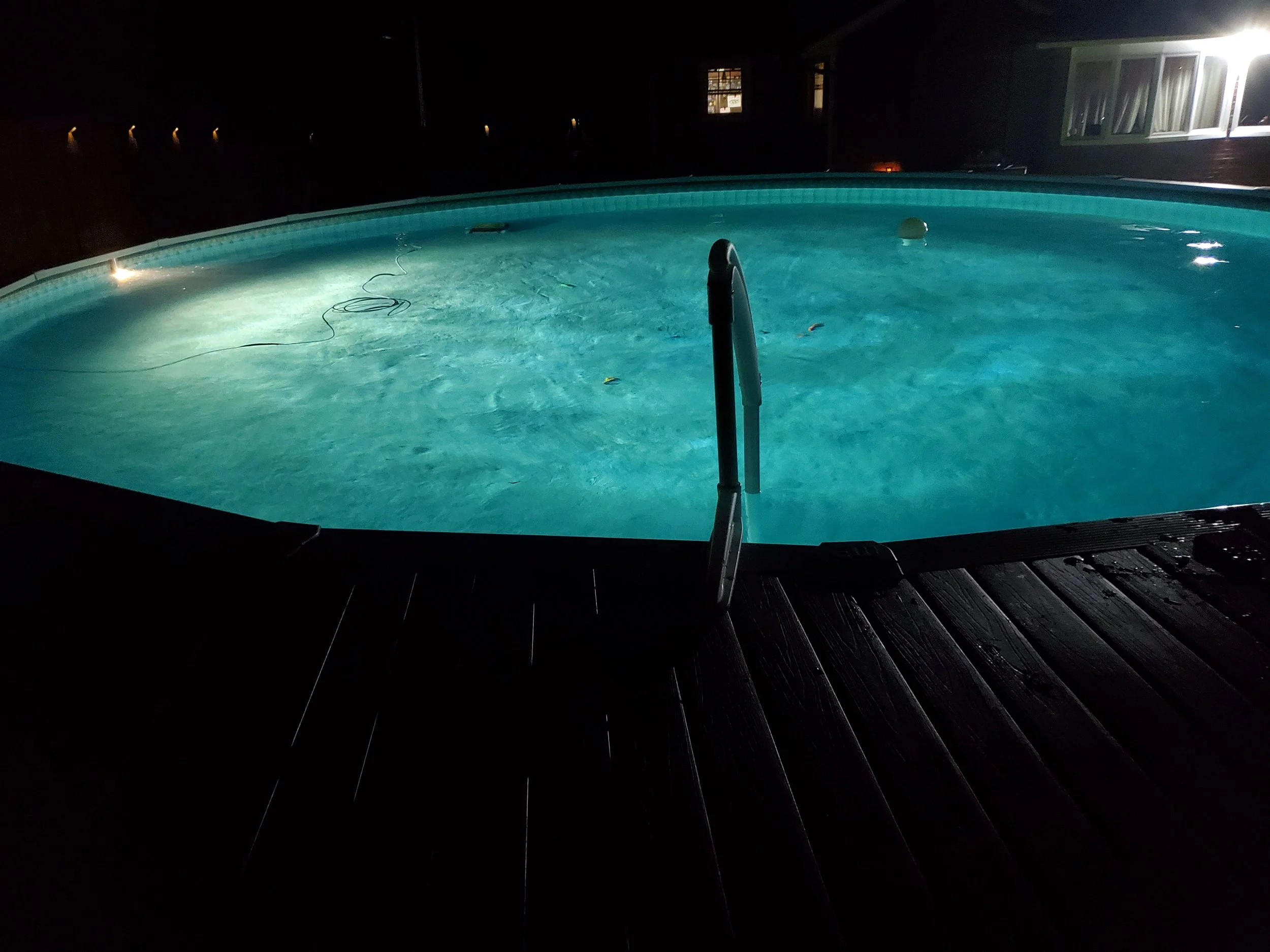 A swimming pool at night with lights illuminating the water, and a ladder at the edge of the pool.