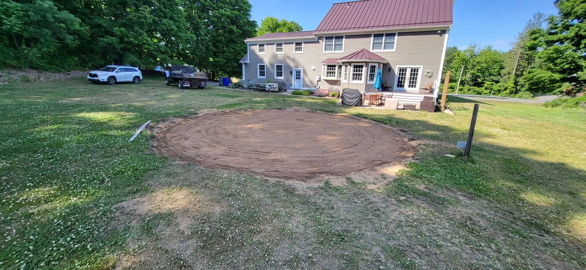 Backyard with a house, parked cars, and a large cleared circular dirt area in the grass.