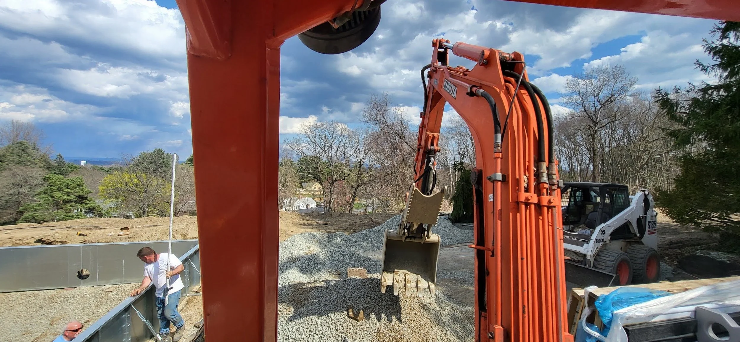 Construction site with a large orange excavator and workers working on a foundation.