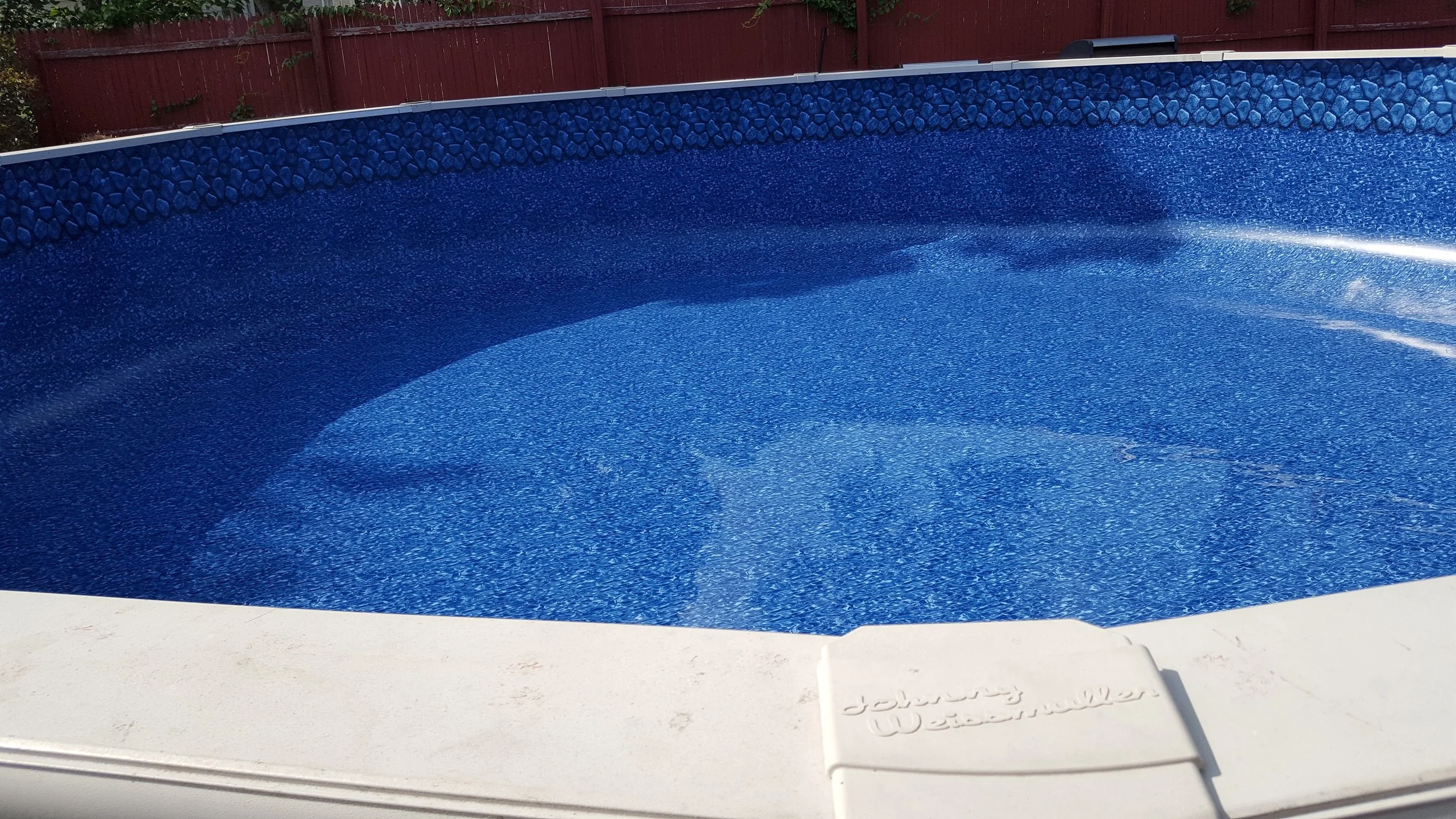 Close-up of a blue textured above-ground swimming pool with a red wooden fence in the background.