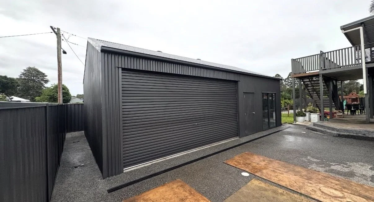 A black metal garage with a large sliding door and a smaller door with glass panels, set on a paved driveway with wooden boards.
