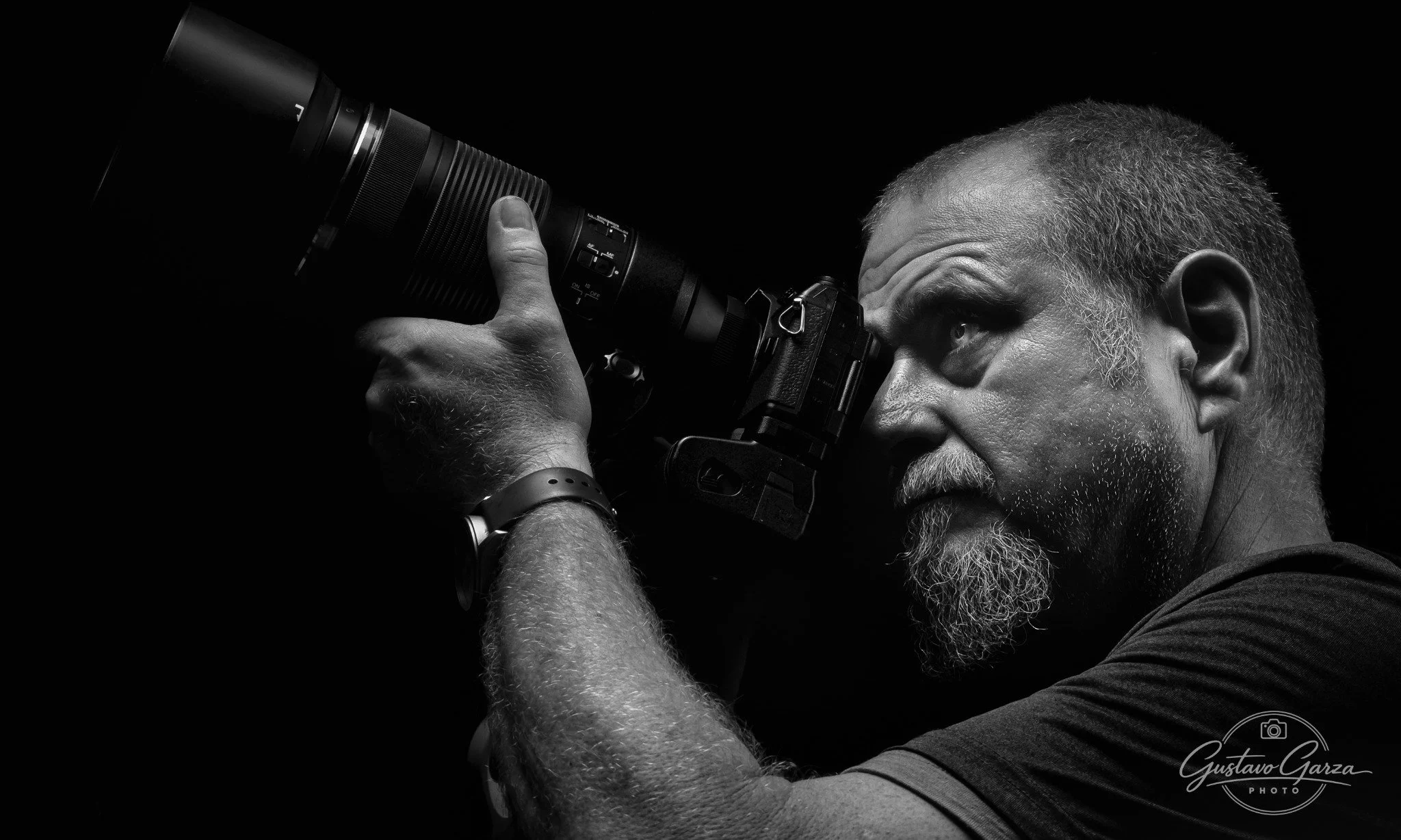 Black and white portrait of photographer Gustavo Garza holding a camera with a telephoto lens