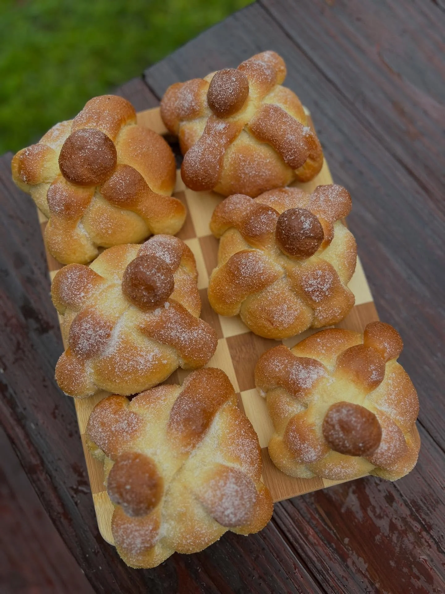 Traditional Pan de Muerto breads arranged on a checkered wooden board outdoors