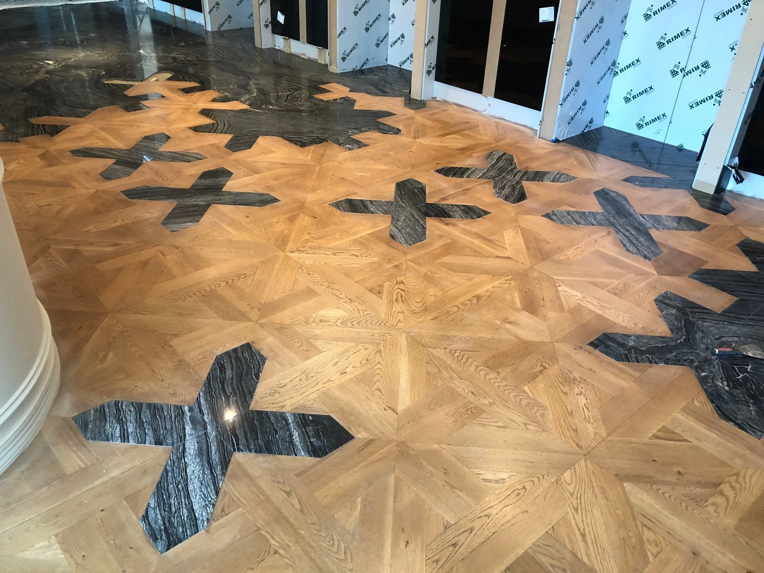Geometric wood parquet flooring with dark marble-like accents in an unfinished interior