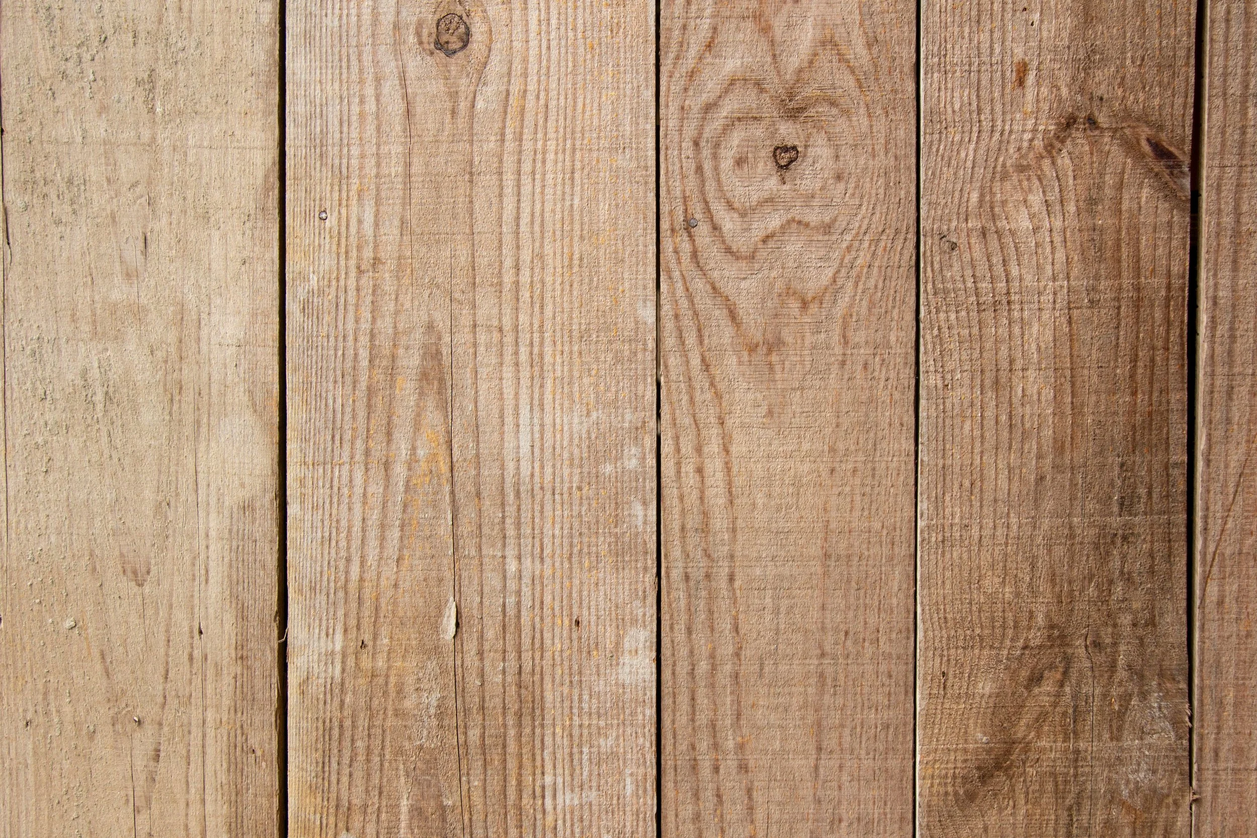 Close-up of weathered vertical wooden planks with visible grain, knots, nail holes, and dark gaps