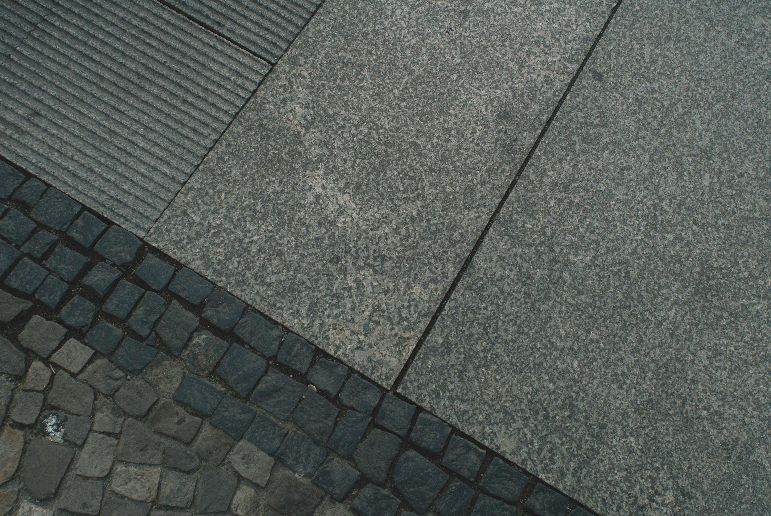 Close-up of gray granite paving slabs, textured stone steps, and dark cobblestones