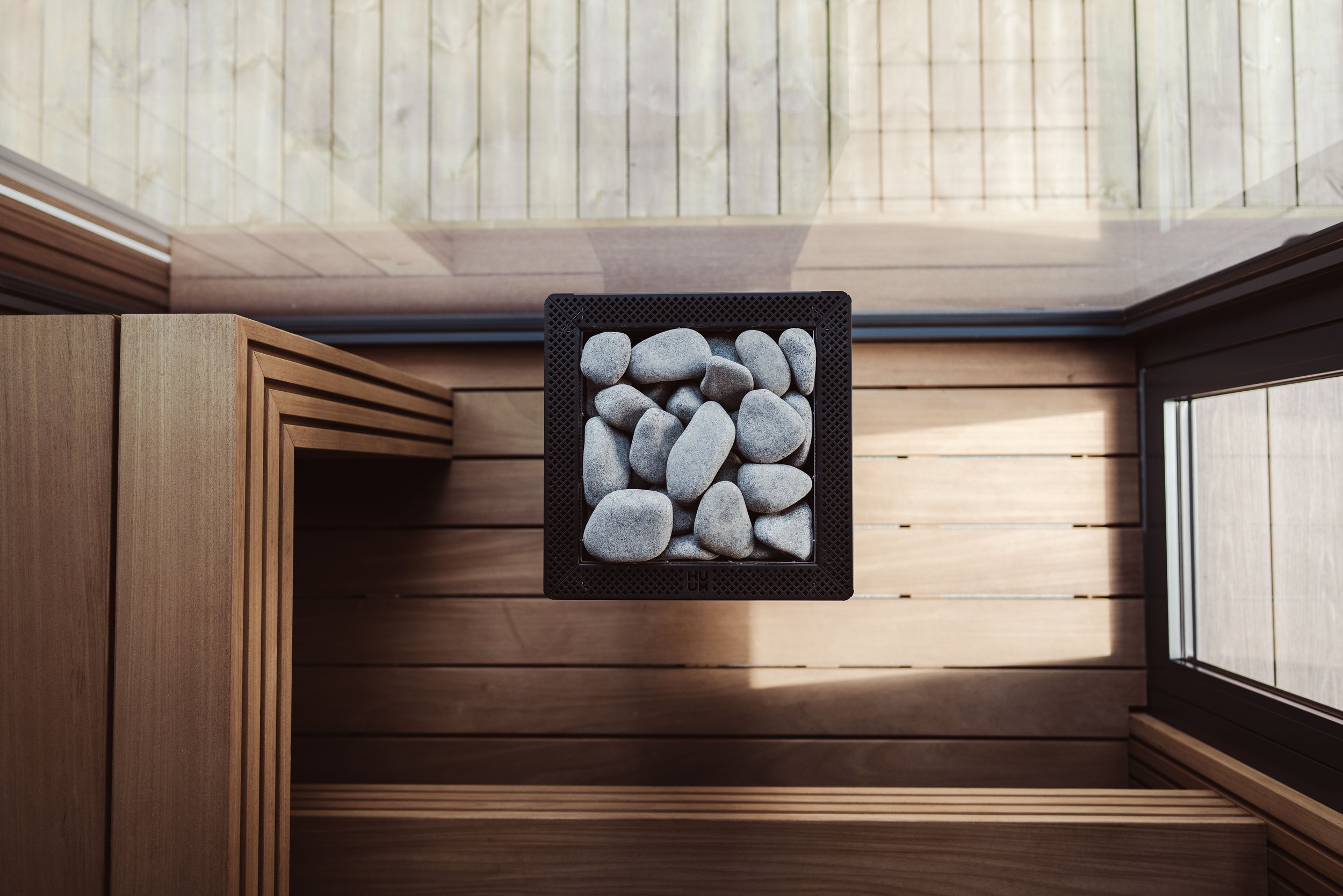 Wood-paneled sauna interior with a wall-mounted electric heater filled with sauna stones