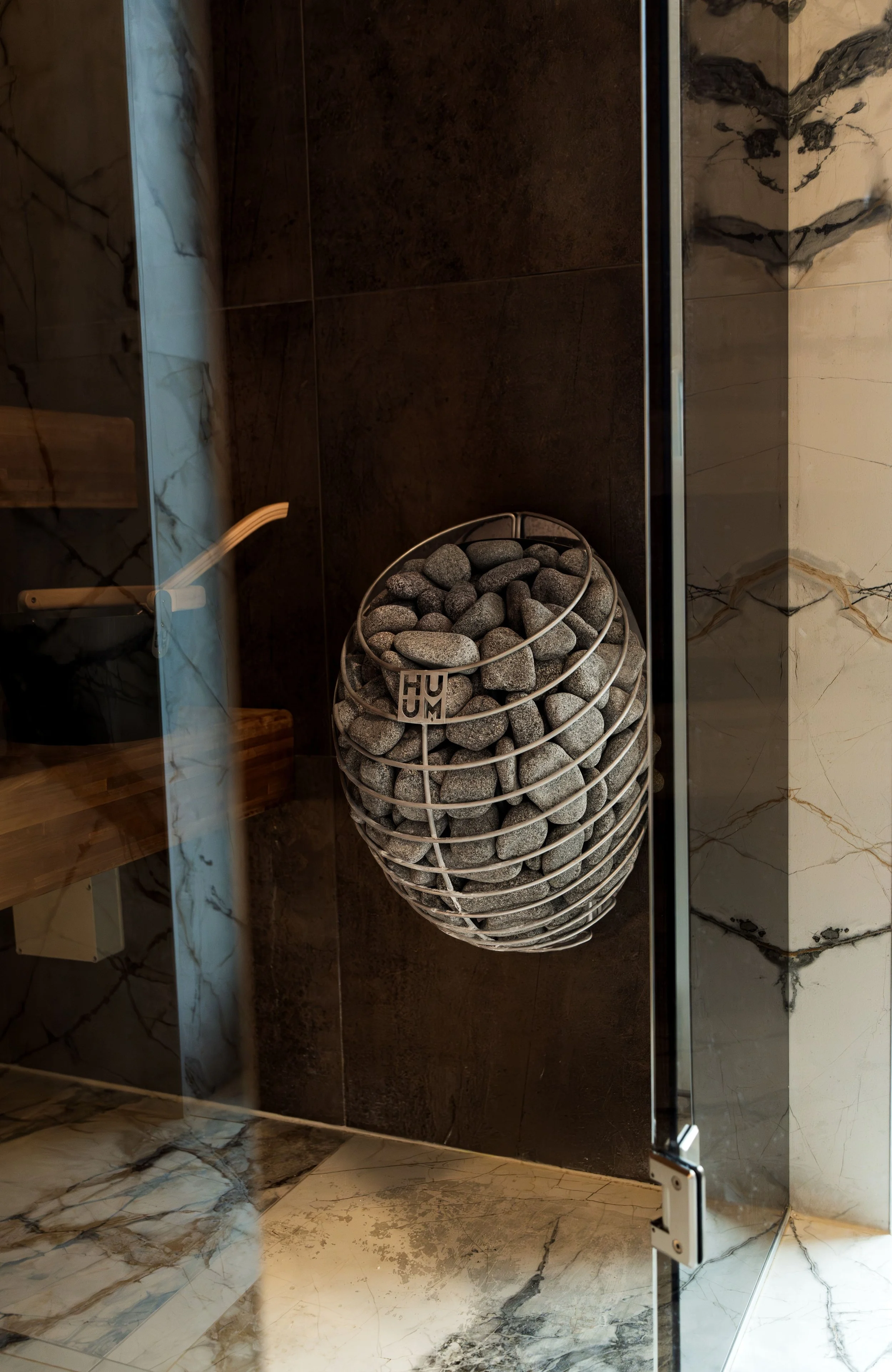 Modern sauna interior with a Harvia stone-filled heater, dark wood walls, and marble tile accents