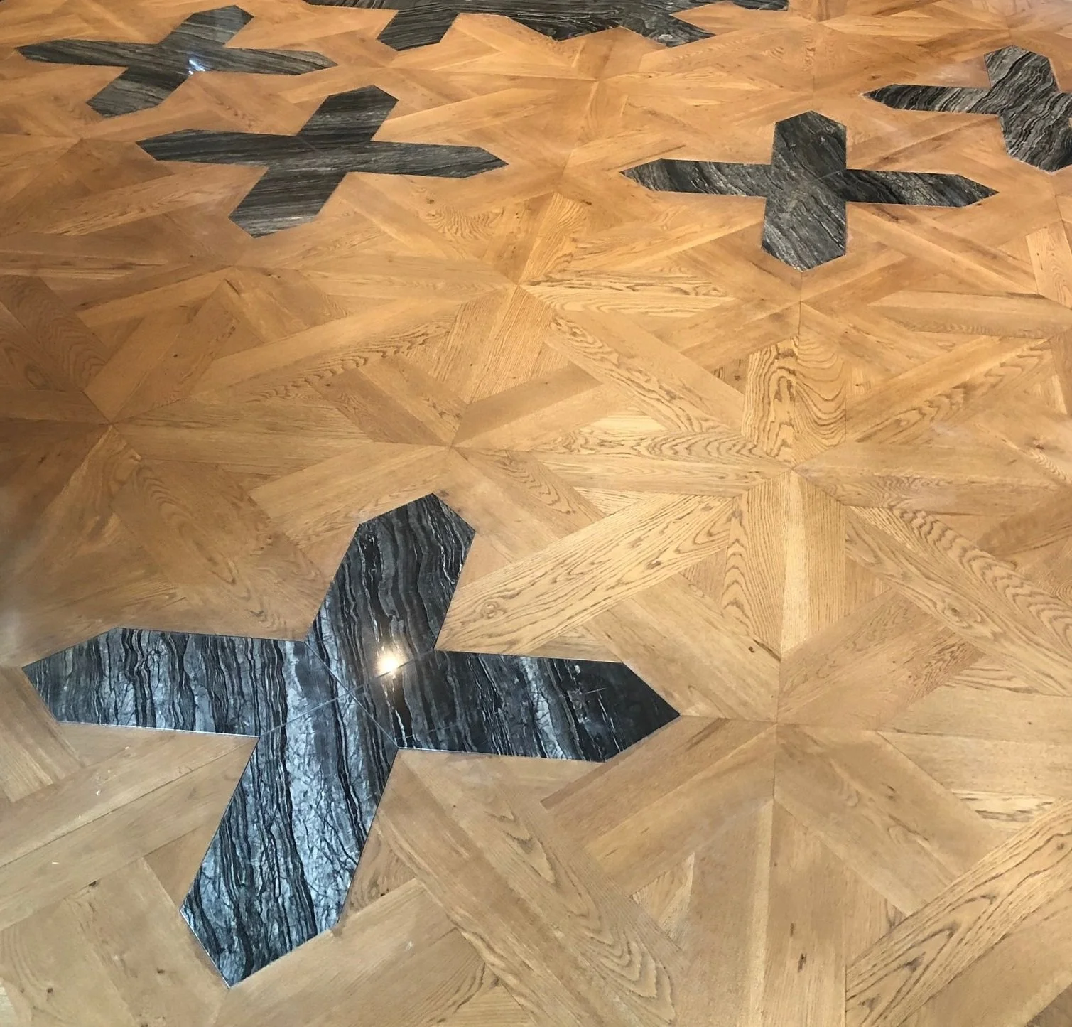 Geometric parquet wood floor with honey-toned oak panels and black veined stone inlays