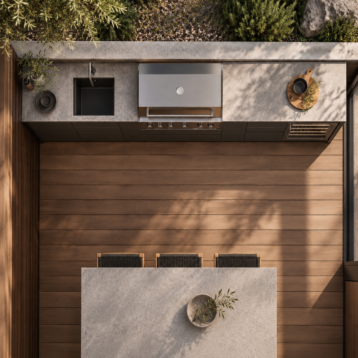 Top-down view of a modern outdoor kitchen with stainless steel grill, sink, wood decking, stone countertops, plants, and dining island