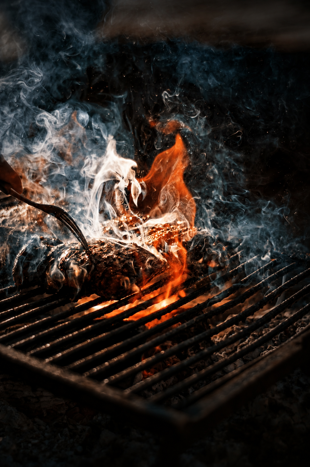 Flaming grilled meat on a barbecue grate with smoke rising
