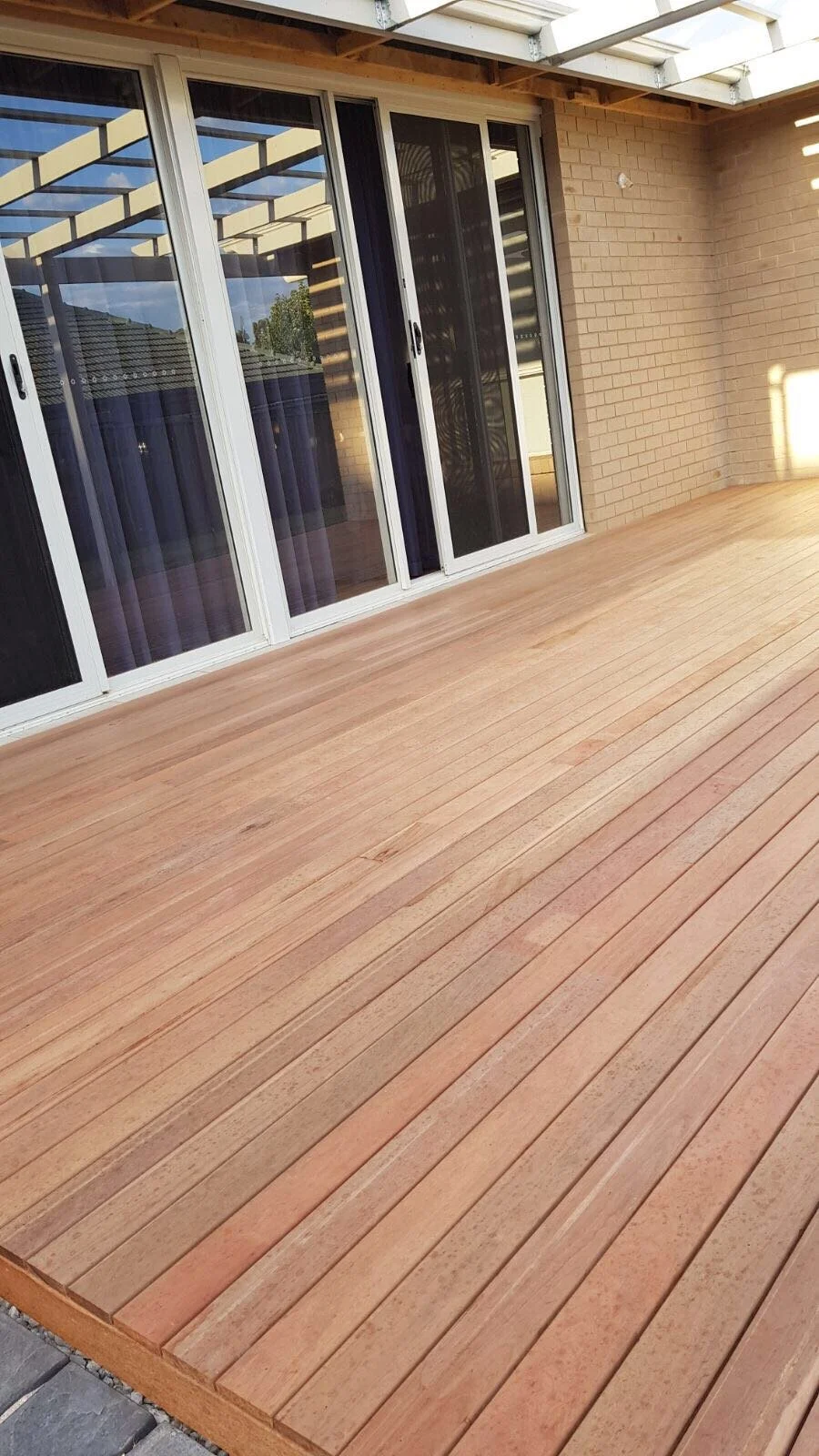 Spacious covered backyard deck with timber flooring, sliding glass doors, and exposed brick walls