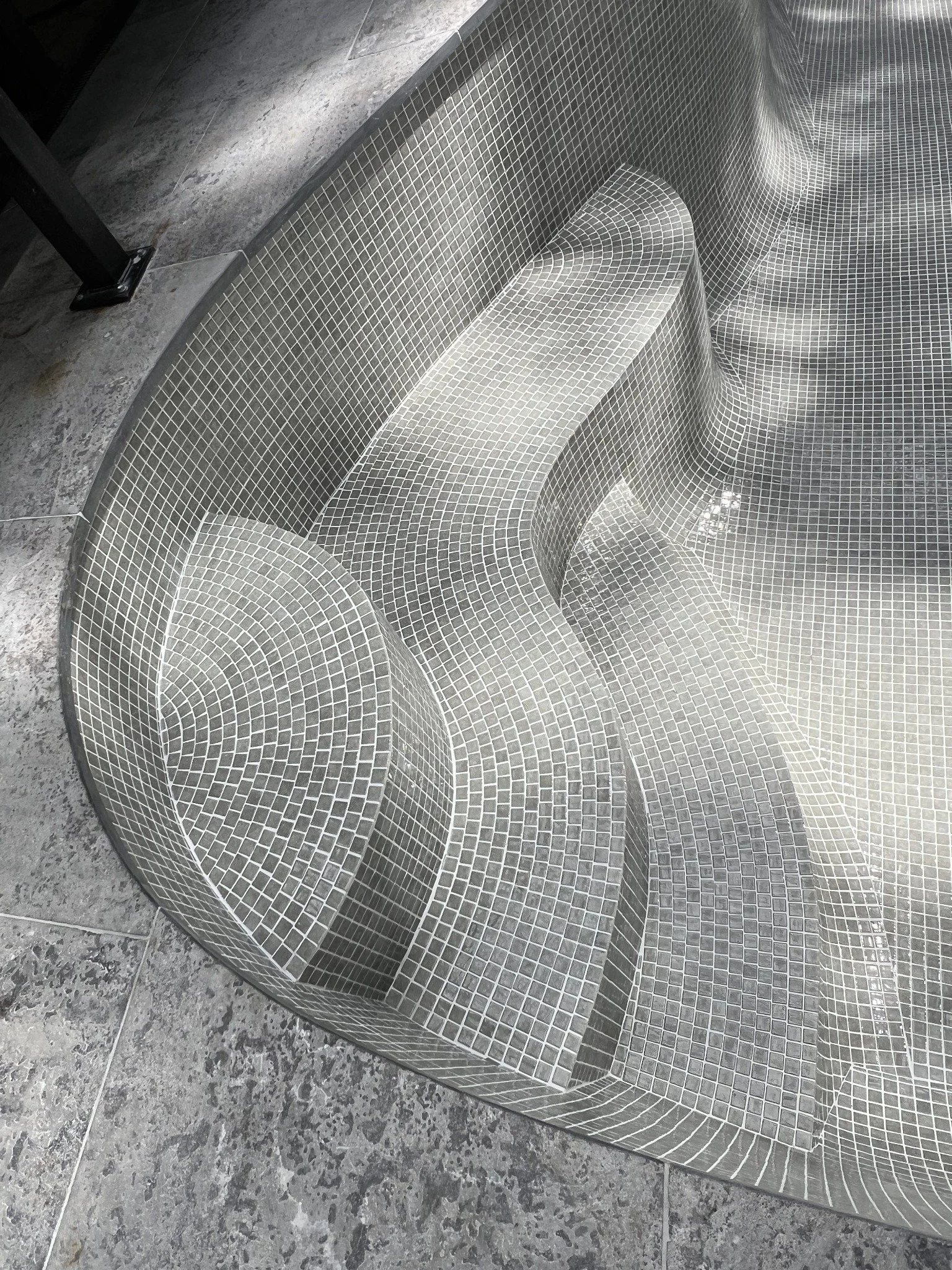Curved gray mosaic-tiled bench and wall in a modern spa or pool area