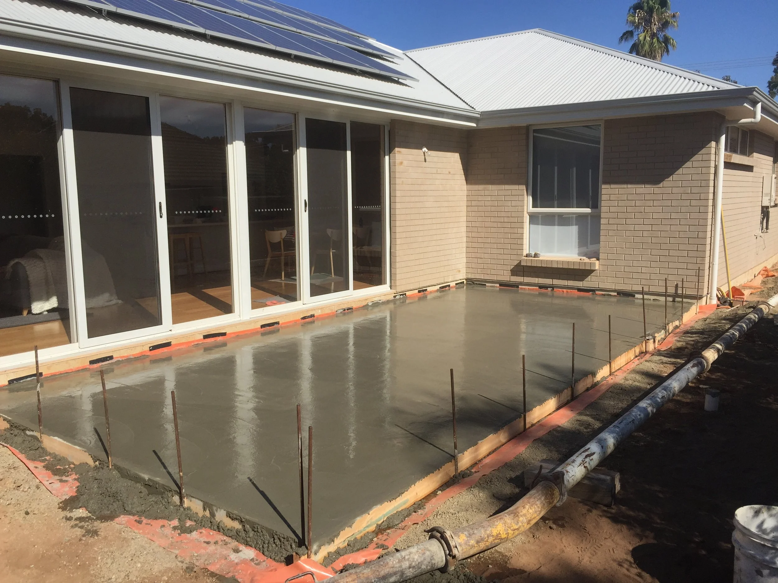 Residential concrete patio being poured beside a brick house with solar panels.