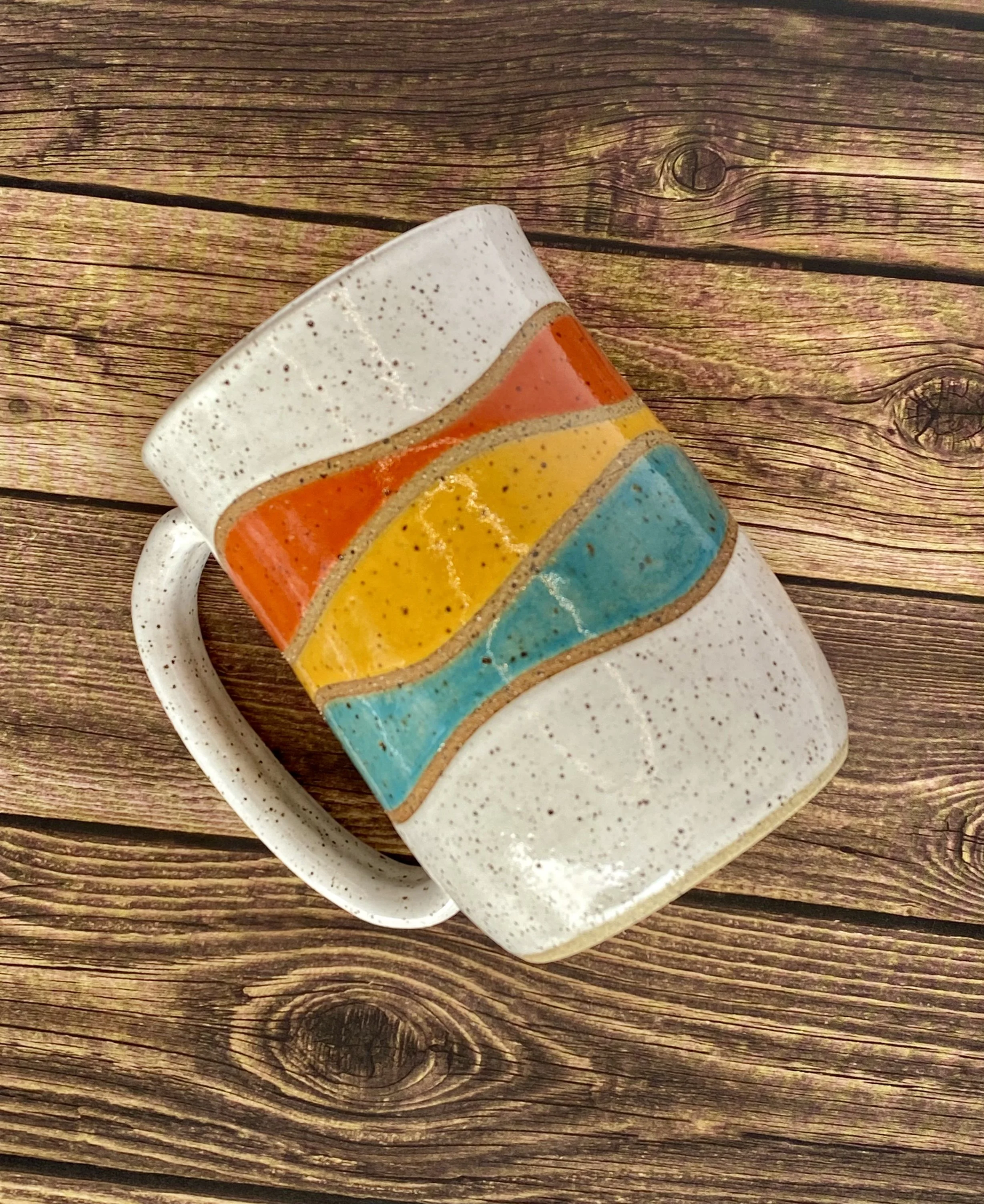 Colorful ceramic mug with hand-carved rainbow stripes against a speckled white clay on top and bottom.