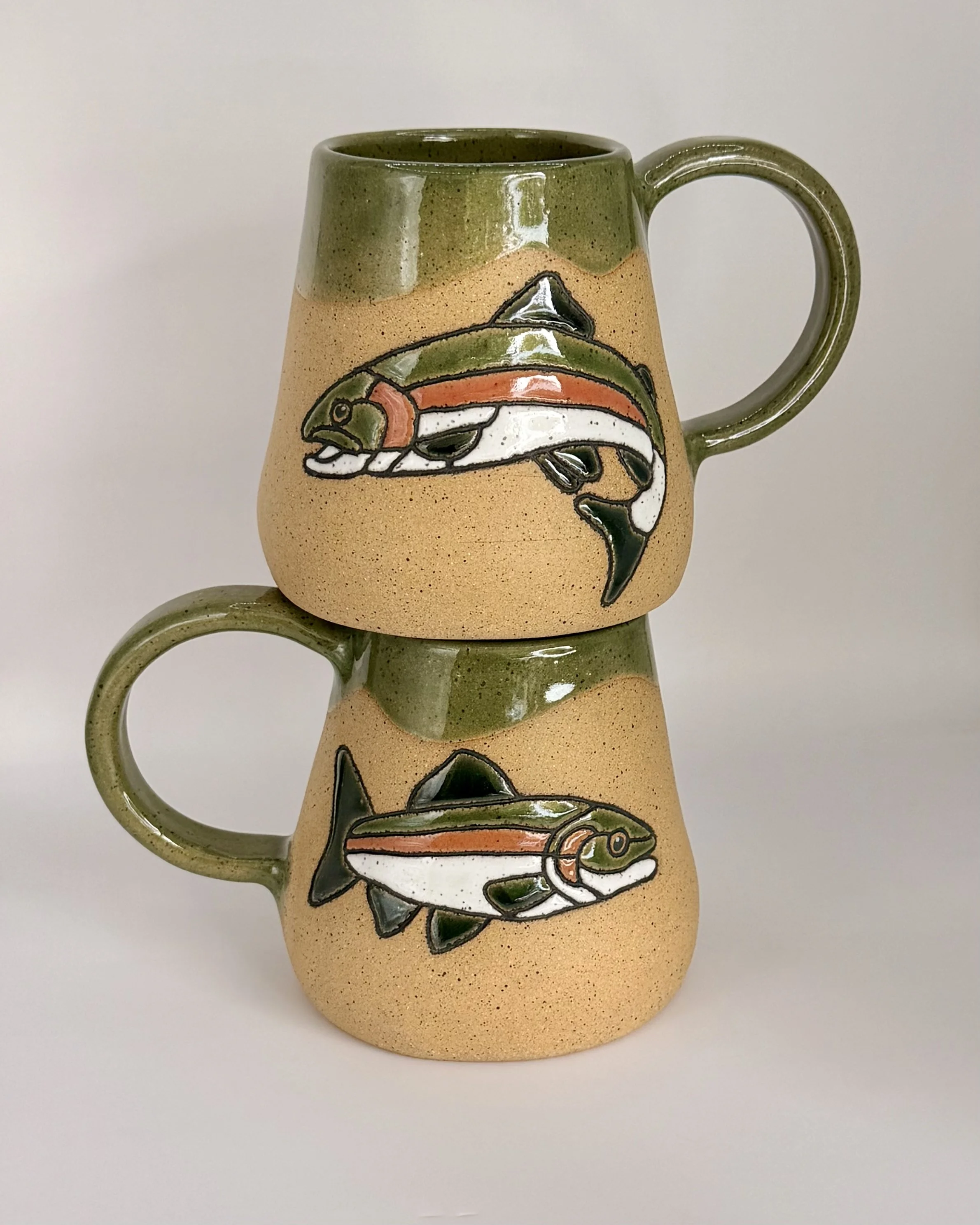 A ceramic hand-built wide bottom mug with a hand-carved image of a colorful trout fish with orange, salmon, white, and green details.