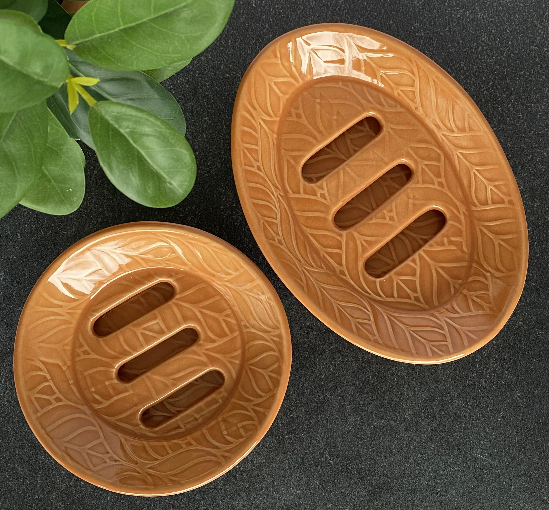 Close-up of orange ceramic self-draining oval and round soap dishes with leaf patterns.