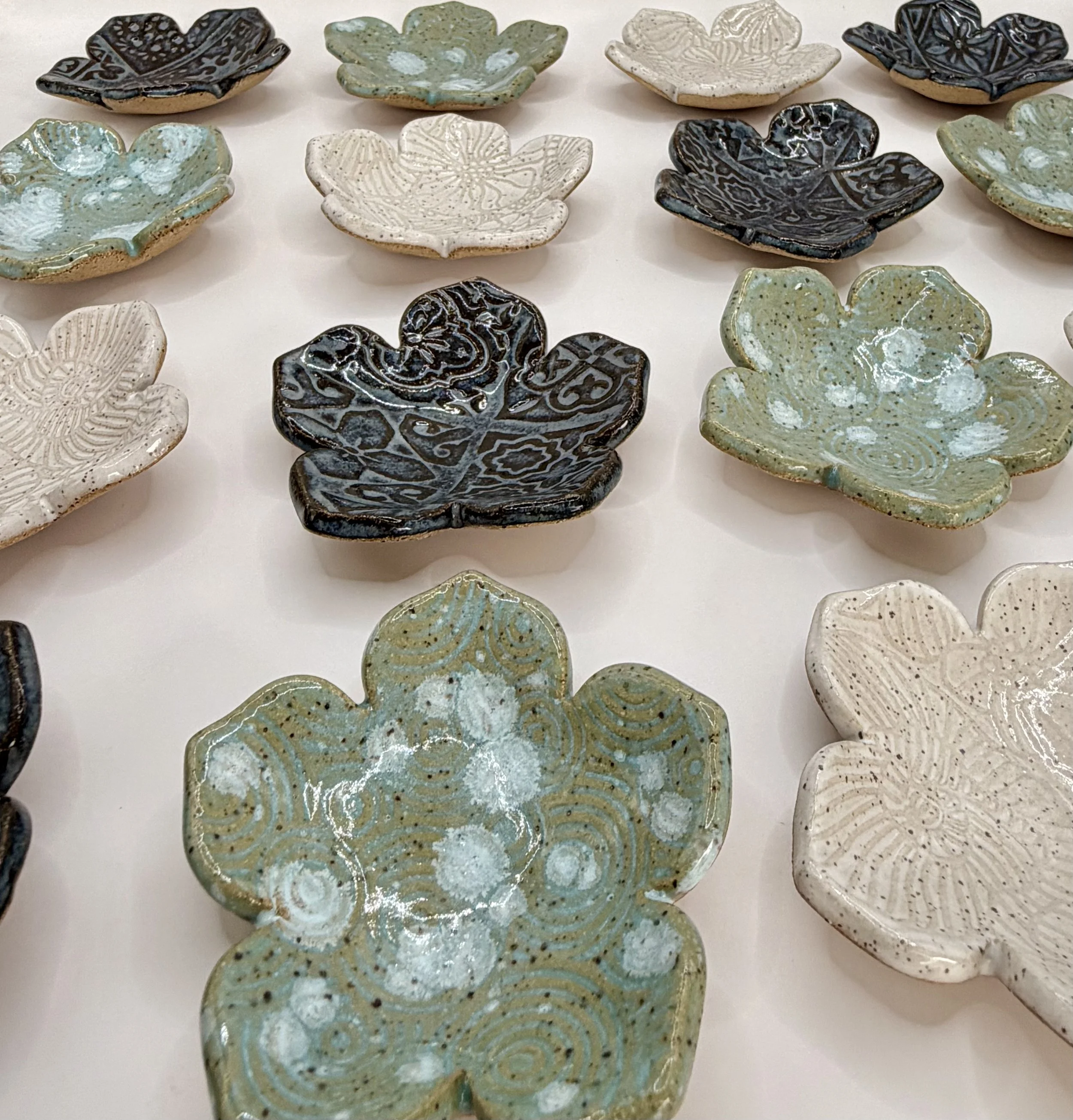 Ceramic flower-shaped jewelry and trinket dishes with intricate patterns in blue, white, and  sea foam green, arranged on a white surface.