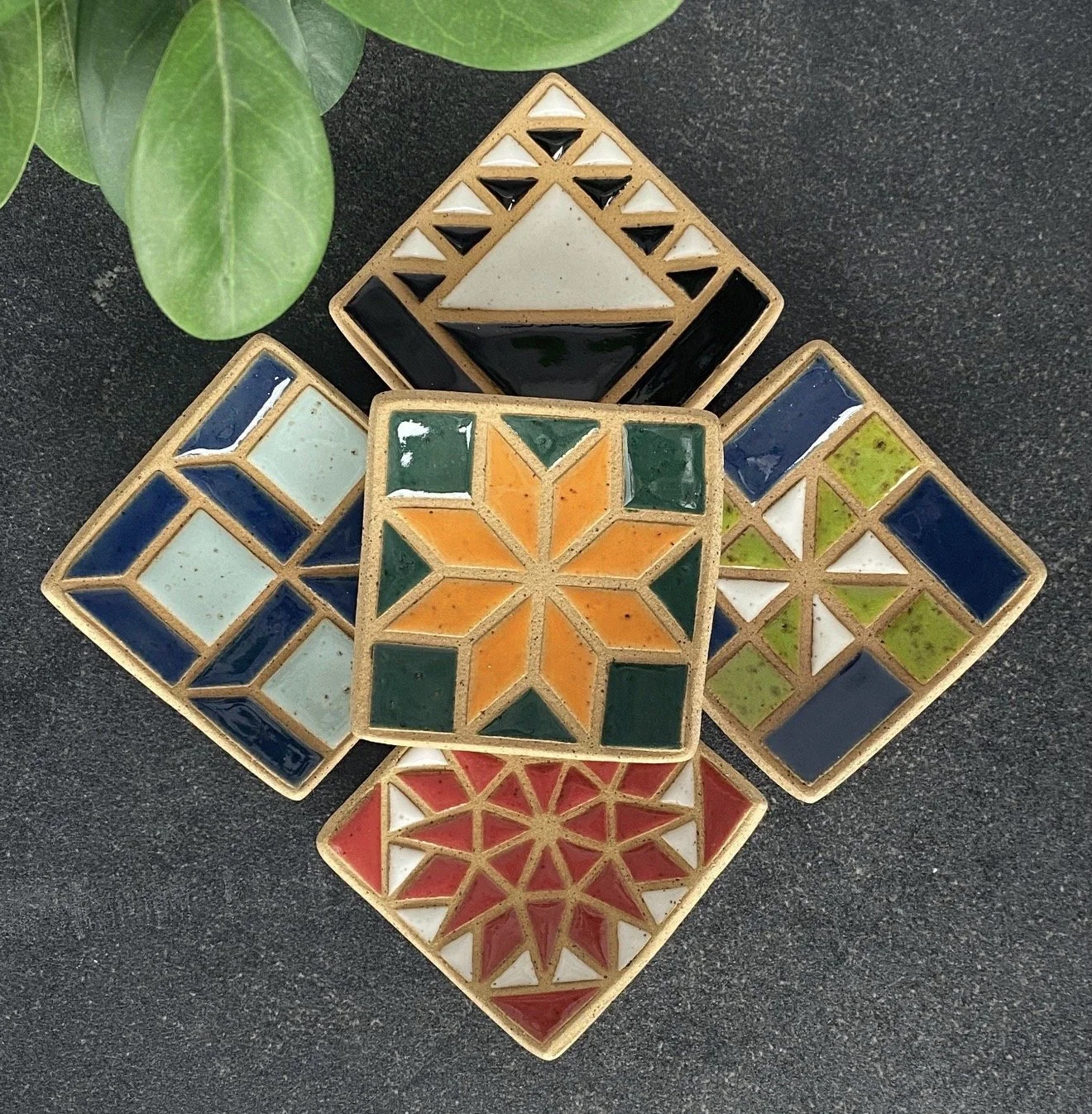 Five square ceramic jewelry dishes with varying geometric quilt patterns and vibrant colors.