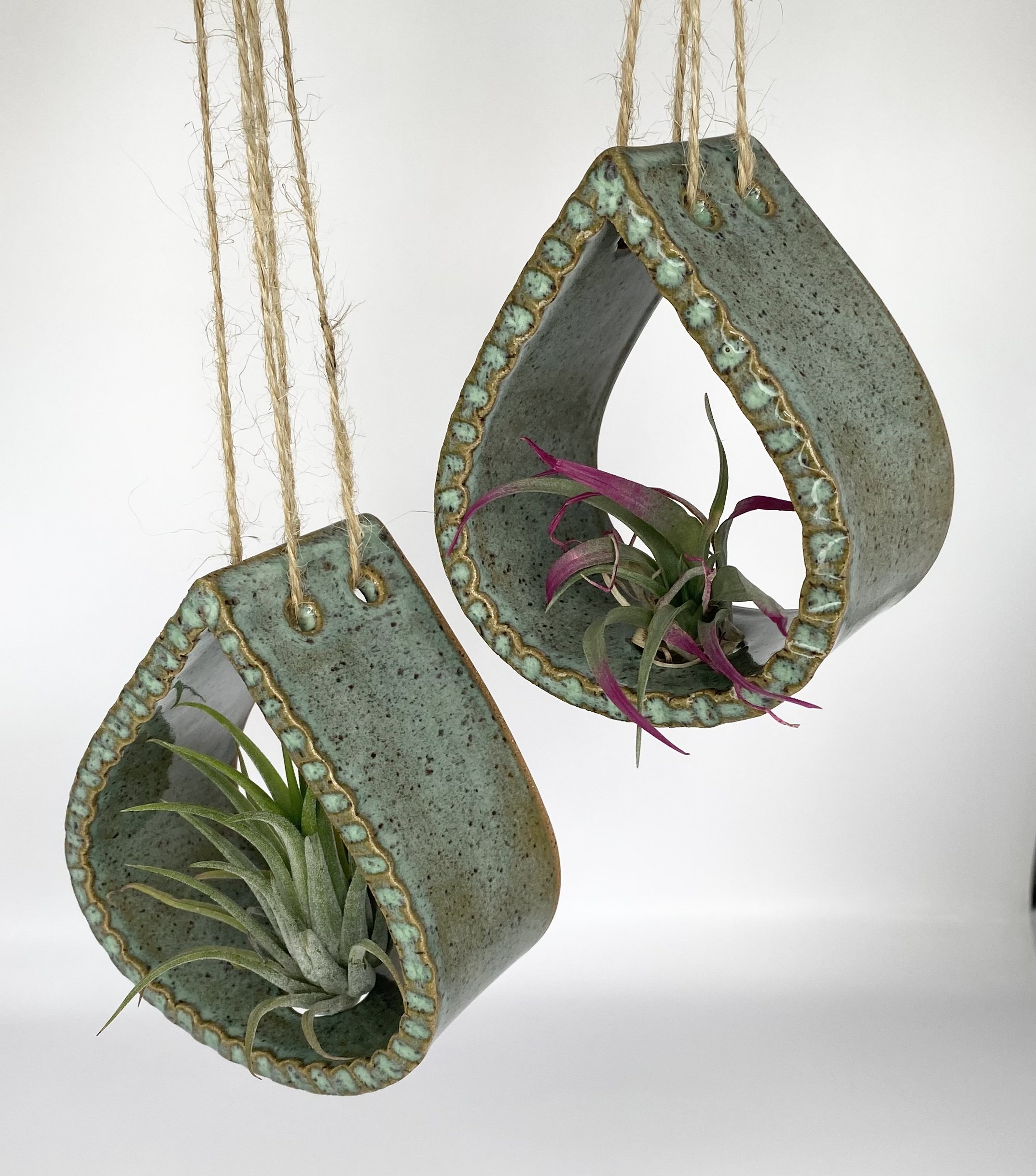 Close-up of two hanging ceramic tear drop airplant holders. Displayed in green glaze and hung with jute string.