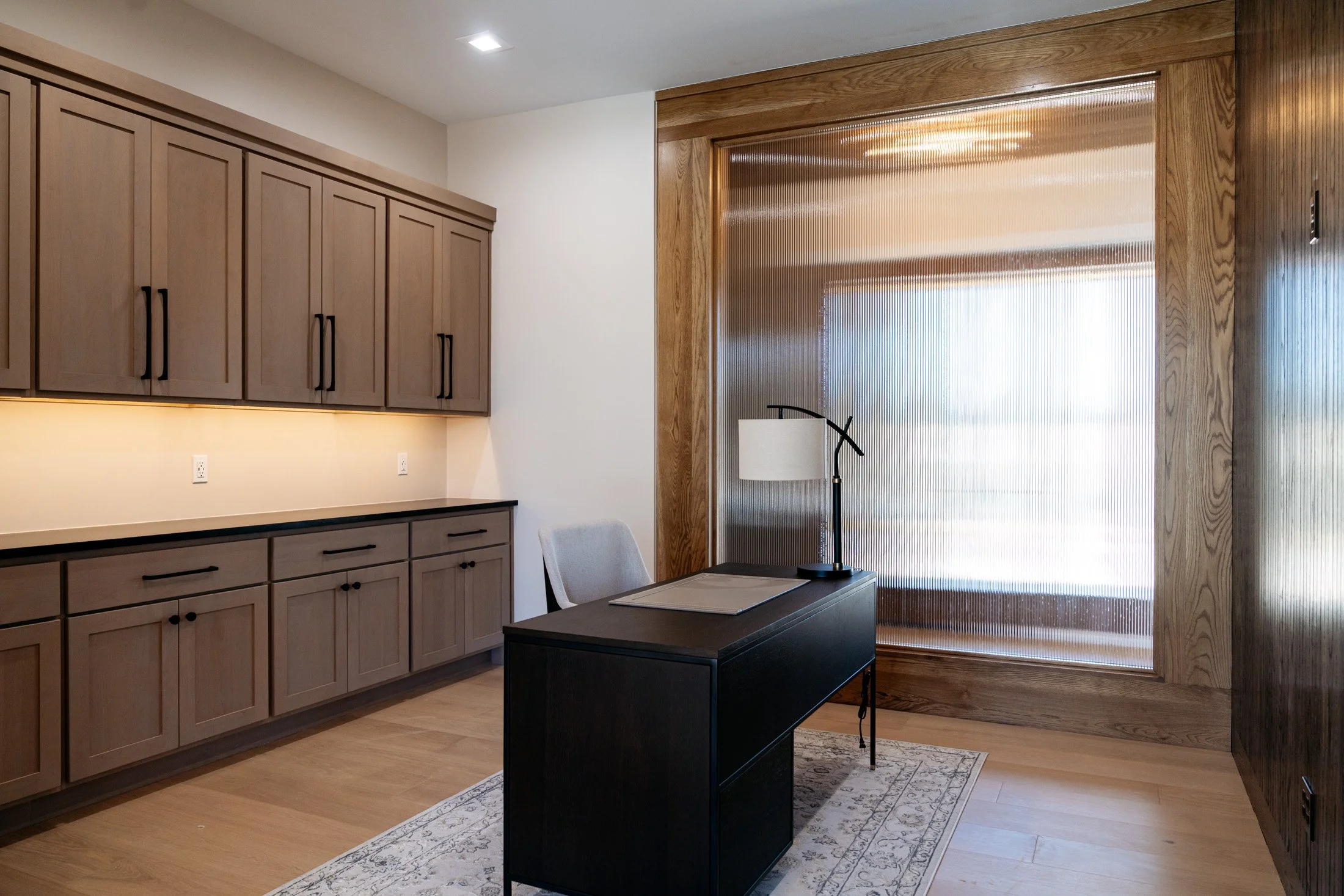 Modern office space with wooden cabinets, a desk with a lamp, and a large textured window.