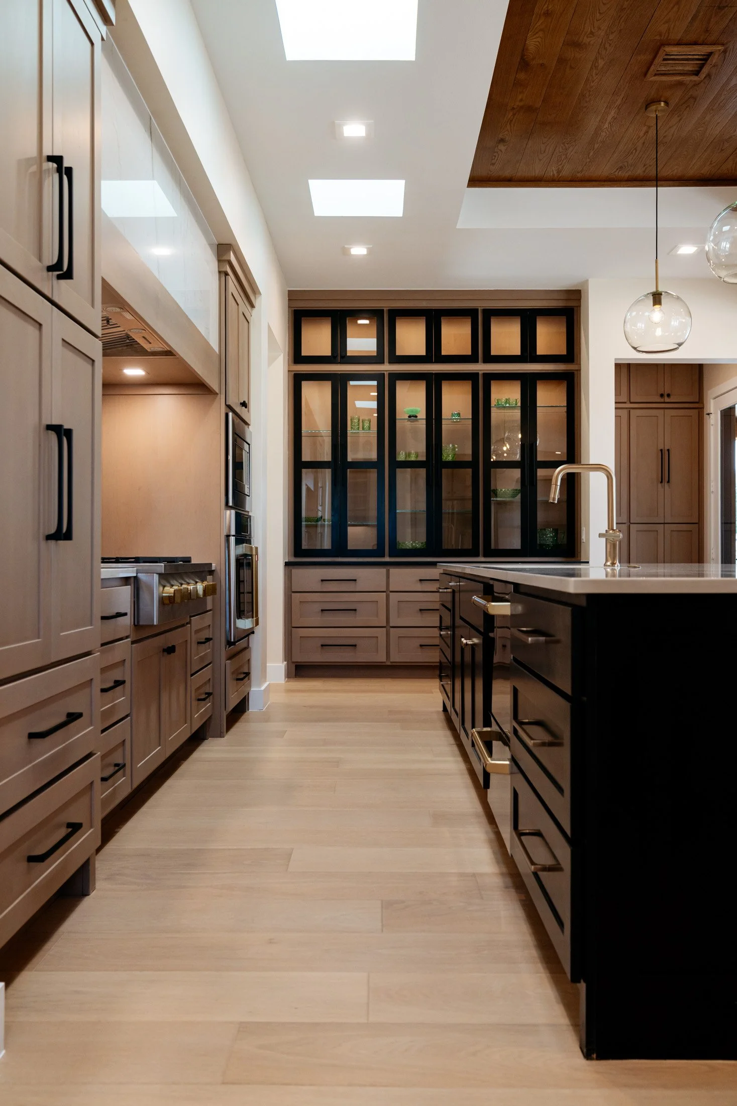 Modern kitchen with light wood cabinets, black accents, a kitchen island, and a glass-fronted cabinet with green decorative items inside.