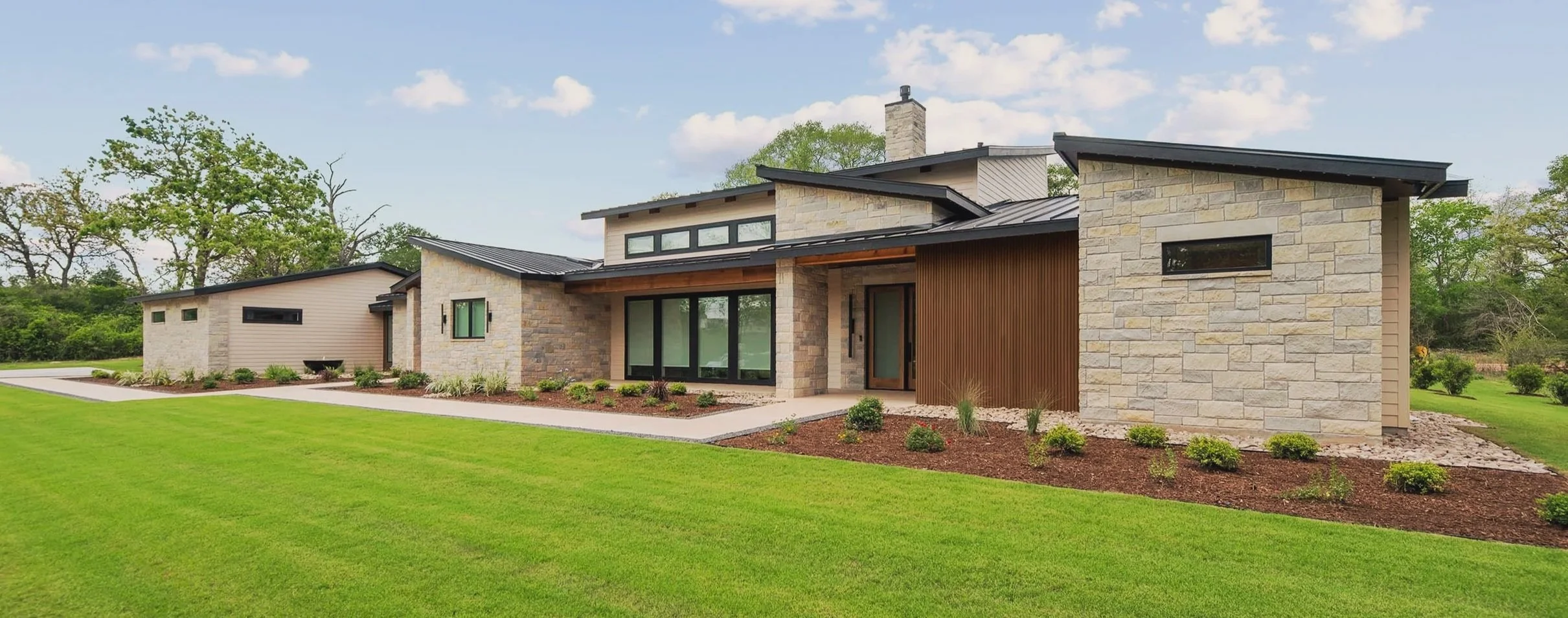 Modern house with stone and wood exterior, large windows, and a well-manicured lawn.