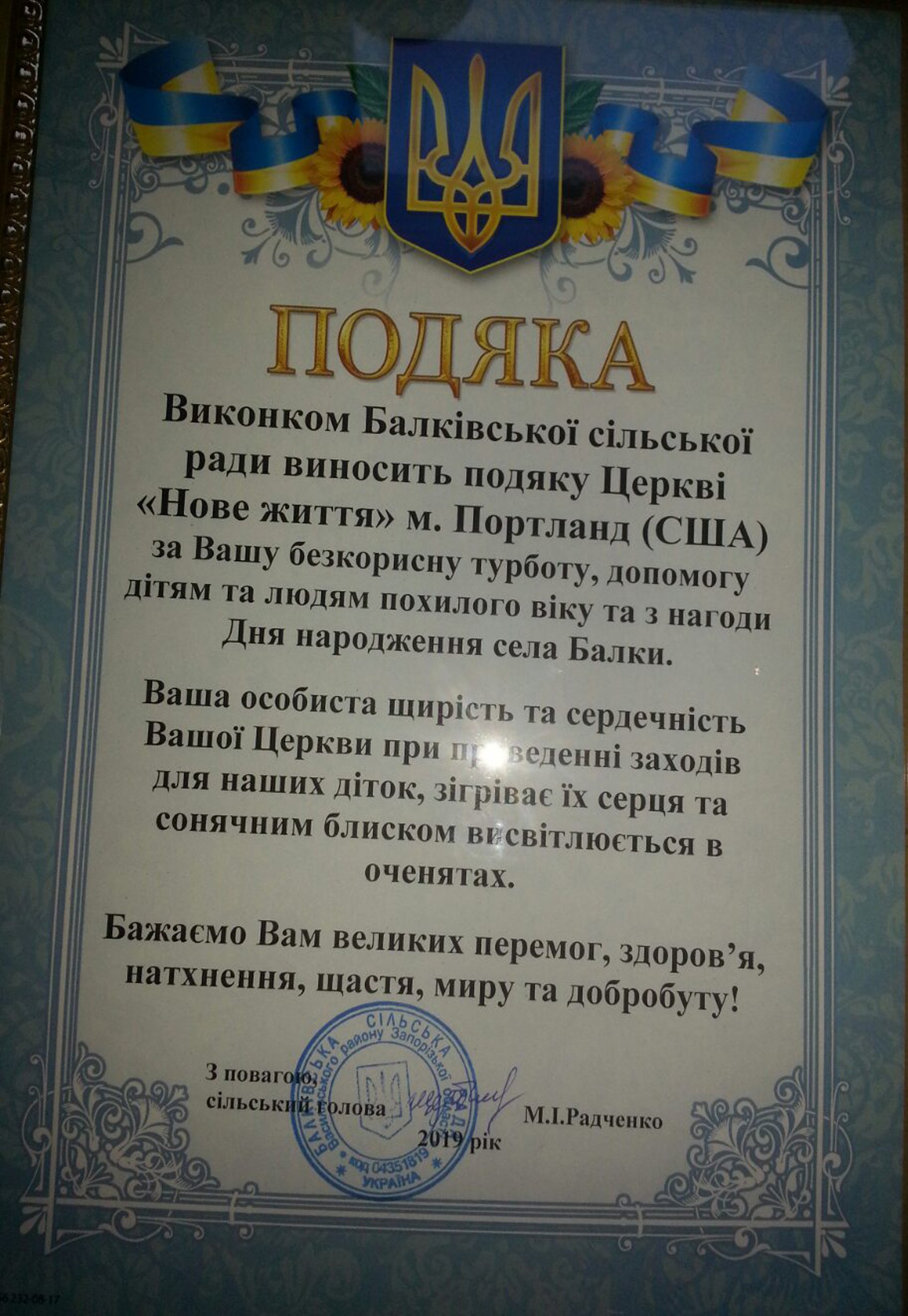 A Ukrainian certificate of appreciation with the national coat of arms, sunflower decorations, and a blue and yellow ribbon, awarded to the Church of 'New Life' in Portland, USA, for caring for children and the elderly.