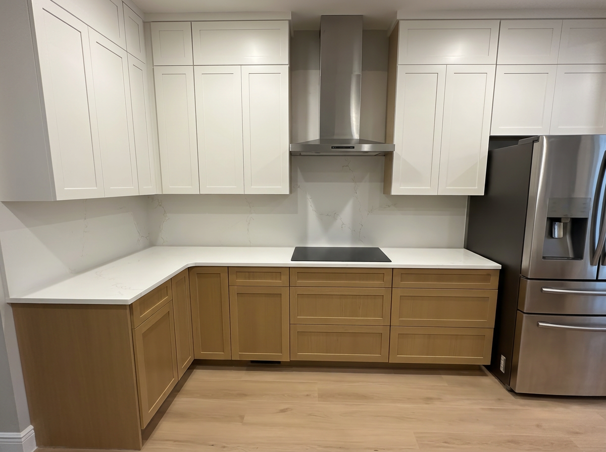 Modern kitchen with white upper cabinets, light wood lower cabinets, a marble backsplash, a black cooktop, stainless steel range hood, and a stainless steel refrigerator.