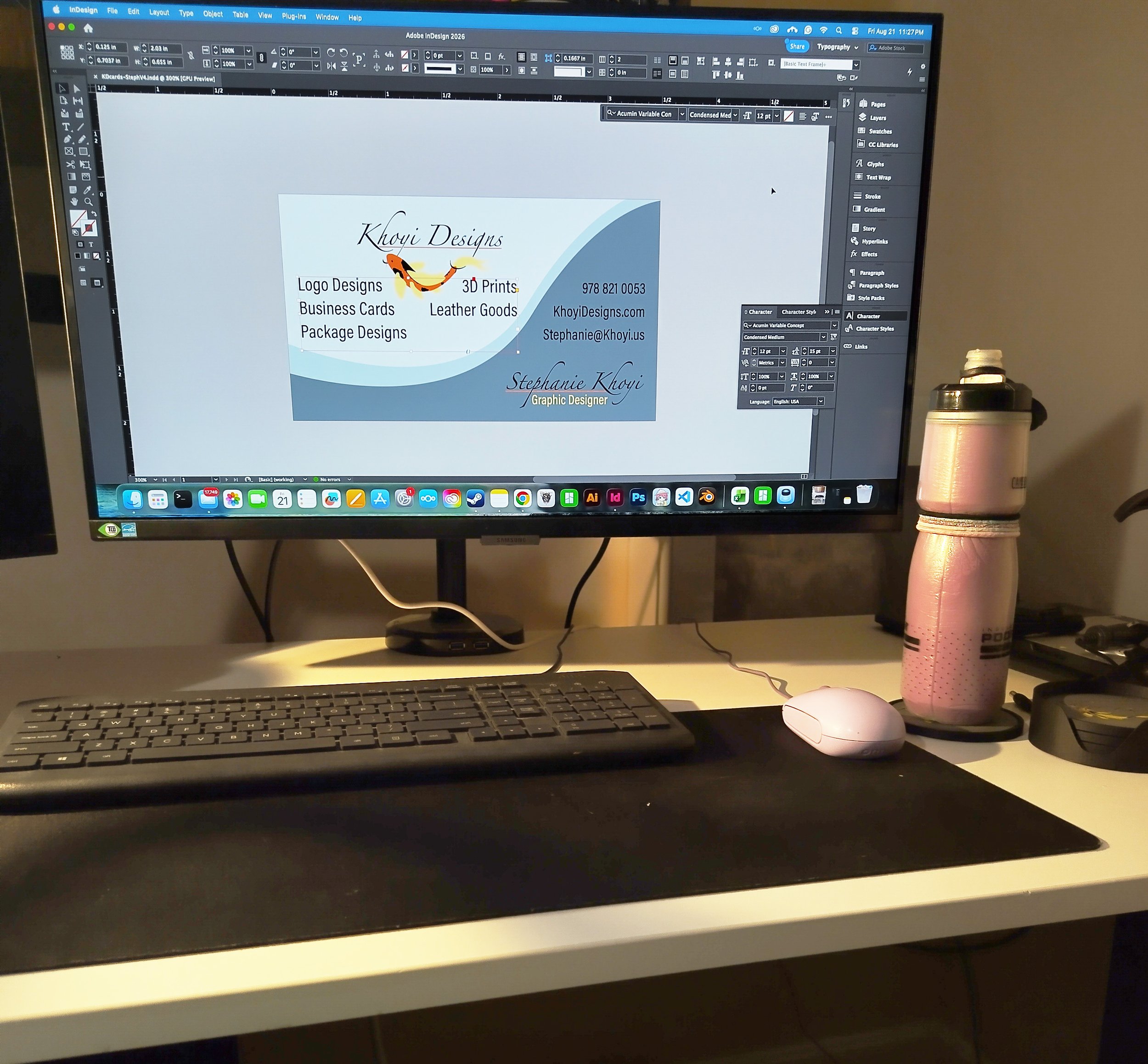 A close up picture of a desk with a computer monitor displaying designing software. The design being worked on is that of the Khoyi Designs business card. A water bottle sits on a 3D printed coaster.