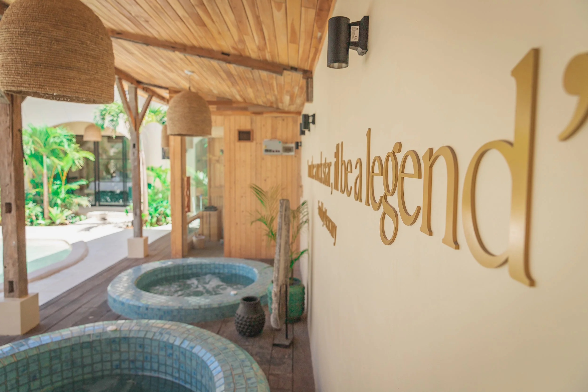 Indoor spa or wellness area with mosaic hot tubs, wooden ceilings and walls, green plants, and decorative hanging lamps.